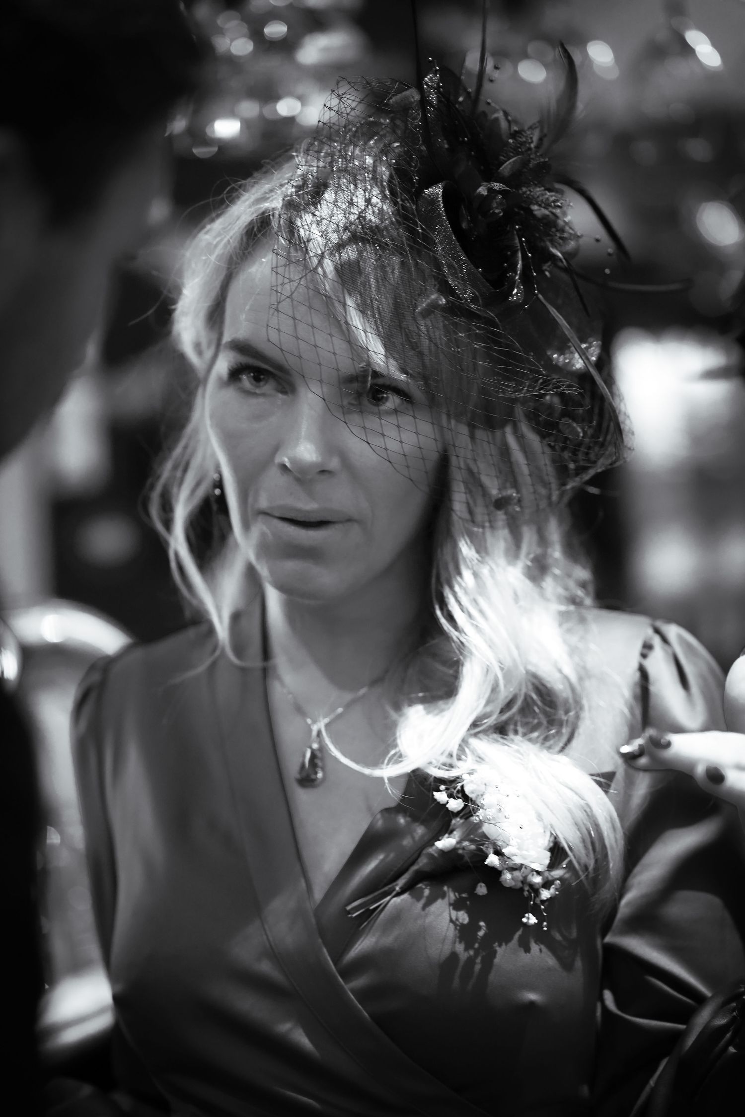 Black and white portrait at a formal event showing an elegant hairstyle with decorative fascinator in a soft bokeh setting.
