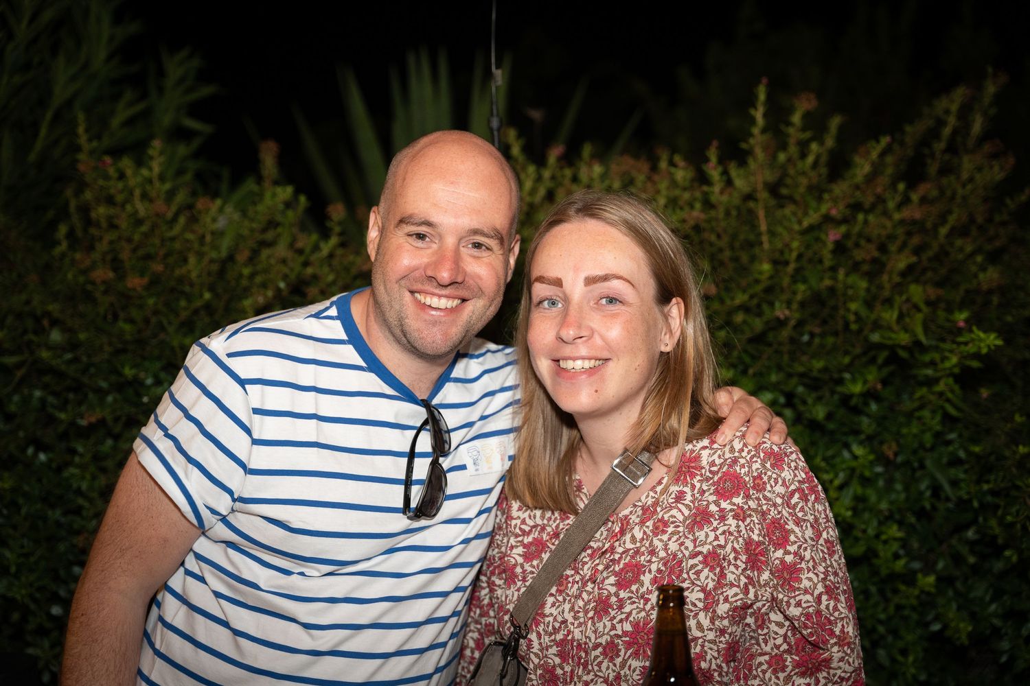 A couple poses together outdoors at sunset against a dark natural background.