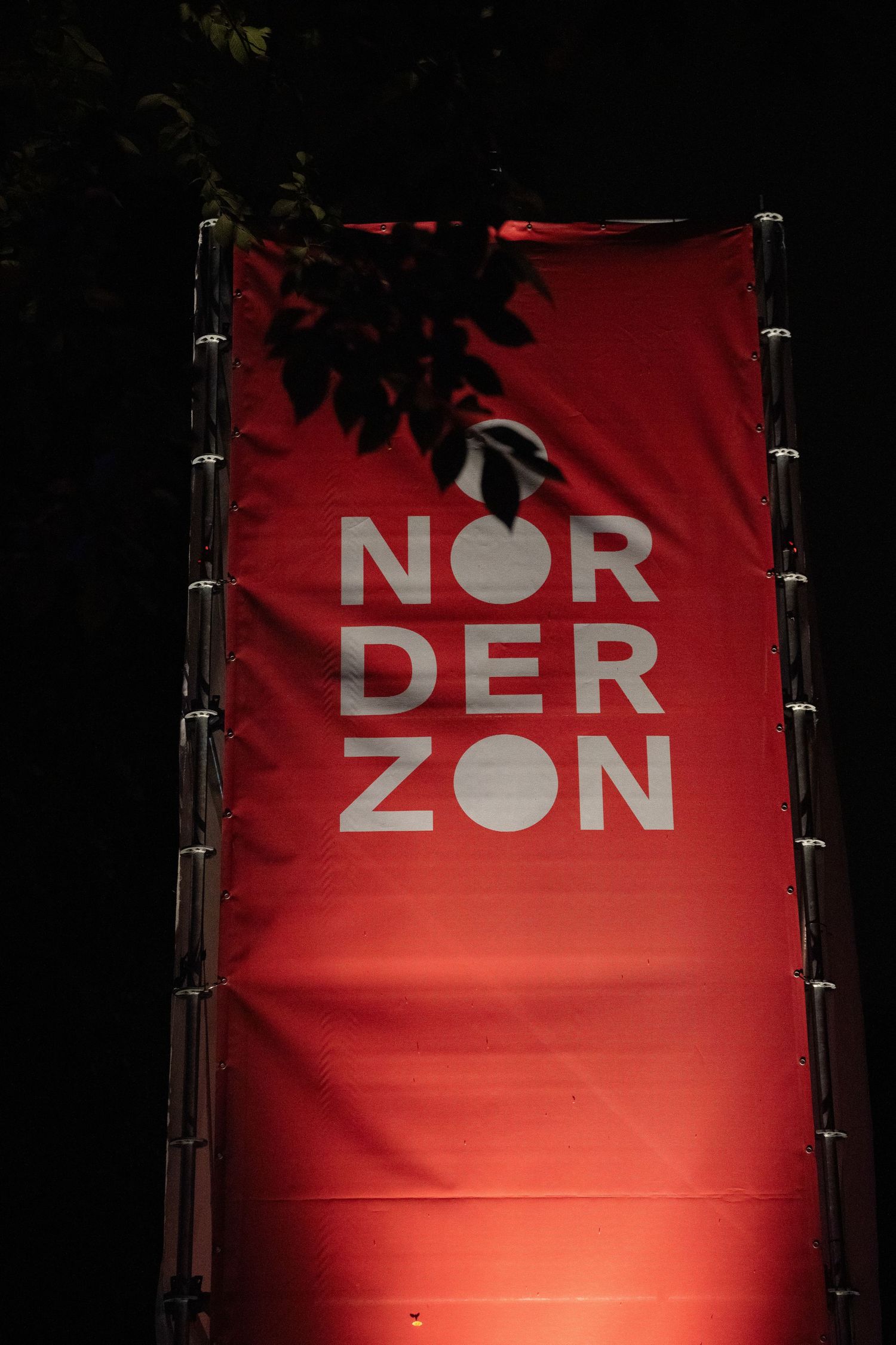 A vertical red banner with the white text 'NORDERZON' displayed against a dark background with tree leaves silhouetted above.