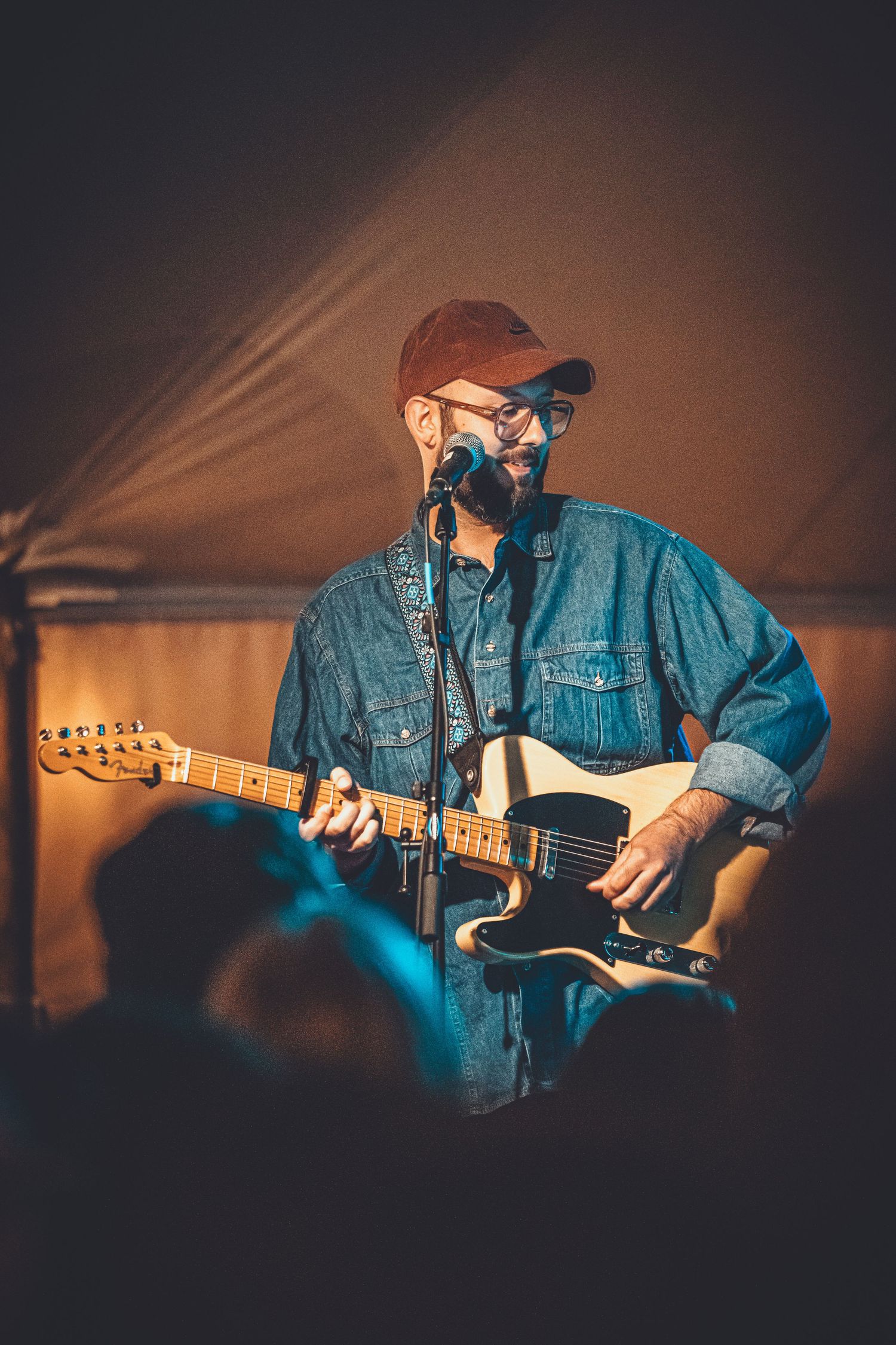A guitarist in denim jacket and beanie performs a dramatic sequence of movements while playing electric guitar in low light.
