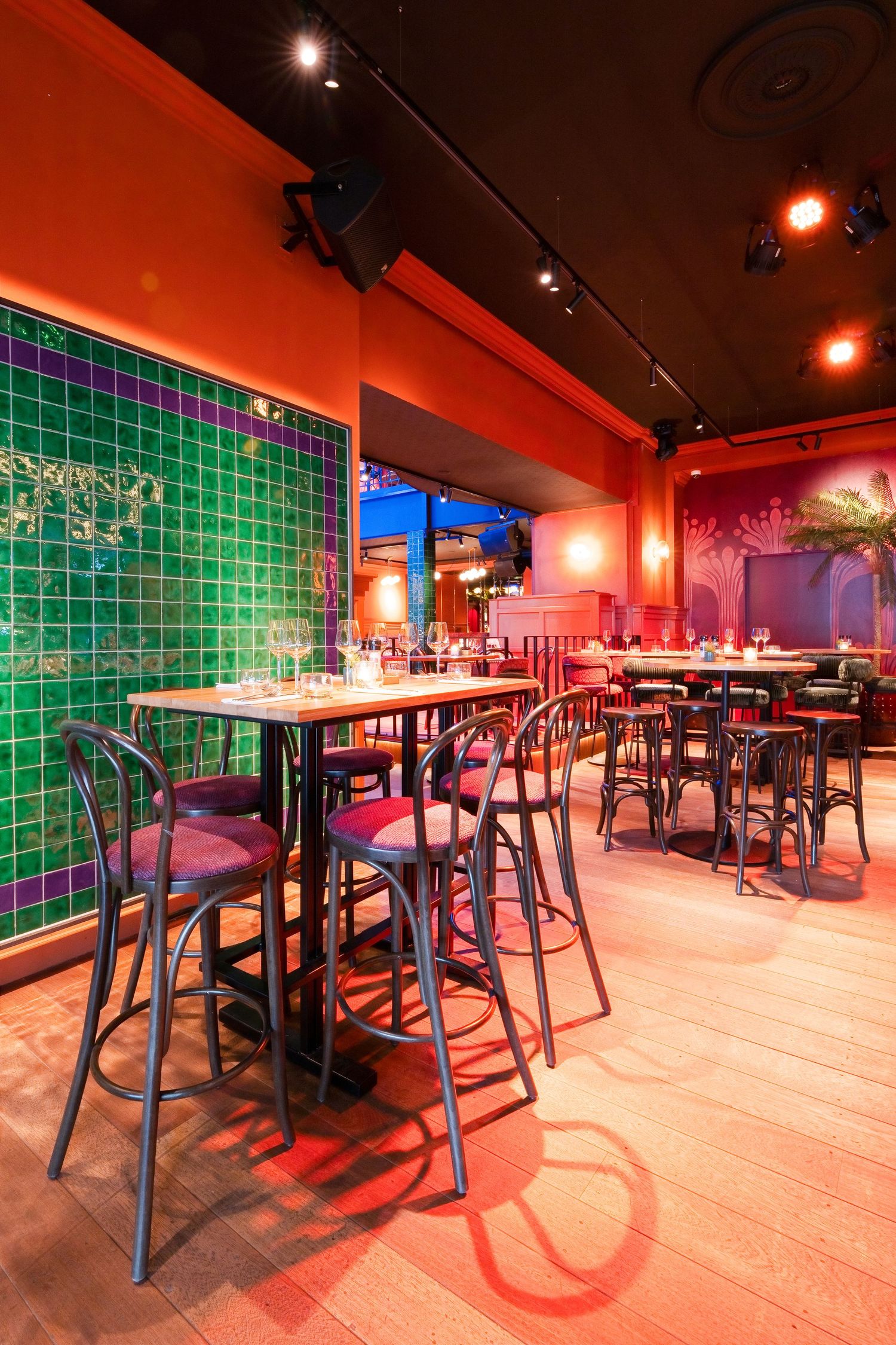 Vibrant restaurant interior with red walls, green tile accent, bar-height tables, and atmospheric lighting.