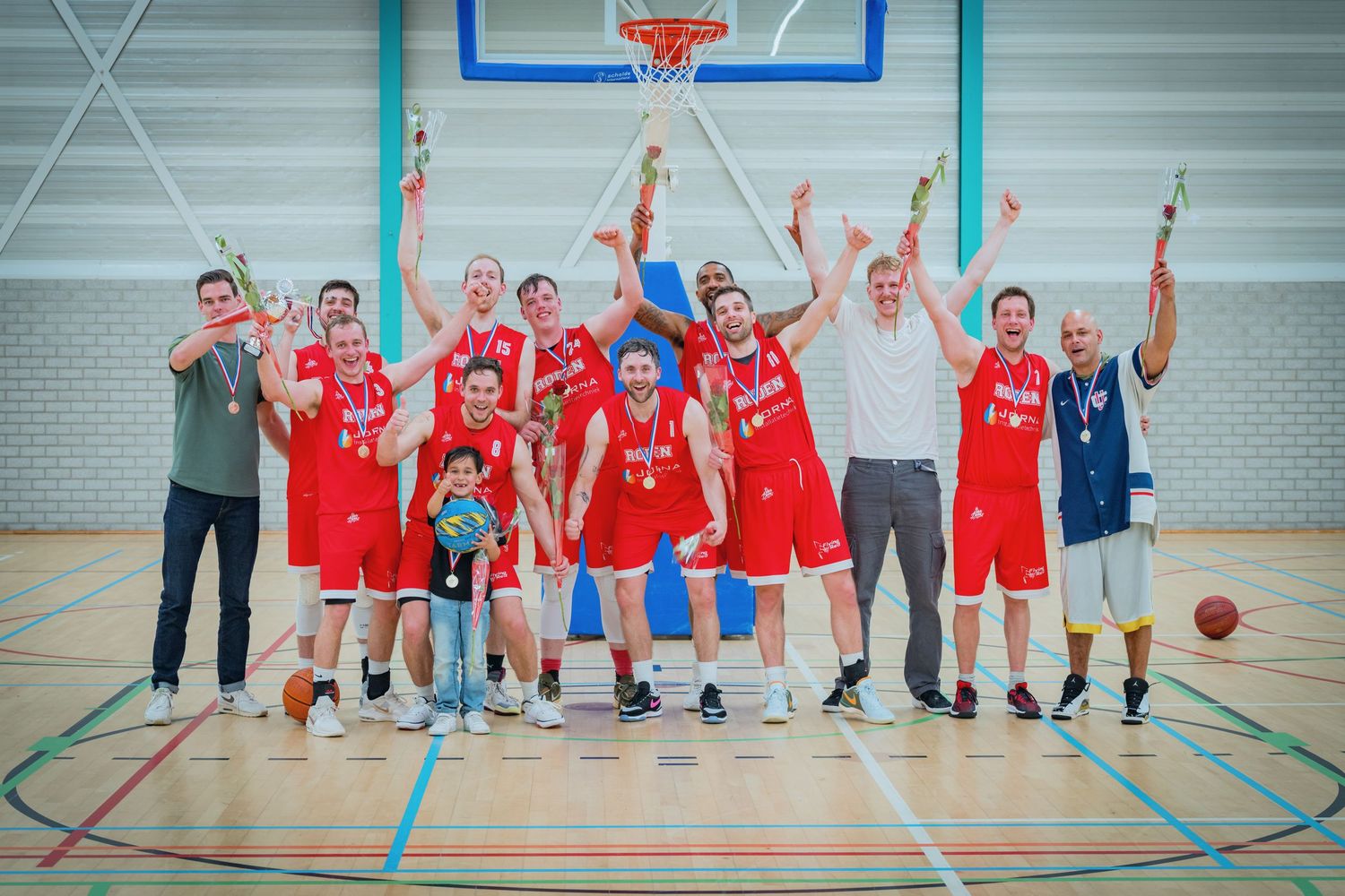 A victorious basketball team in red uniforms celebrates together on an indoor court after their game.