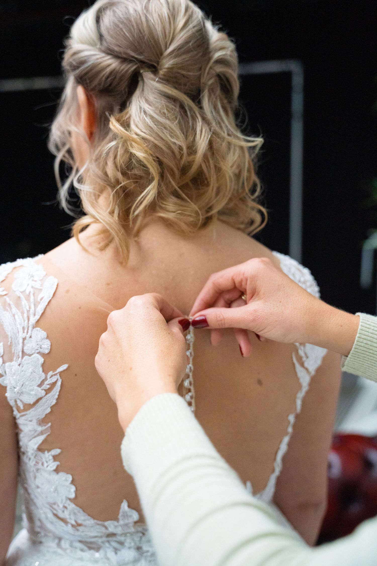 Close-up of hands fastening buttons on lace wedding dress back.