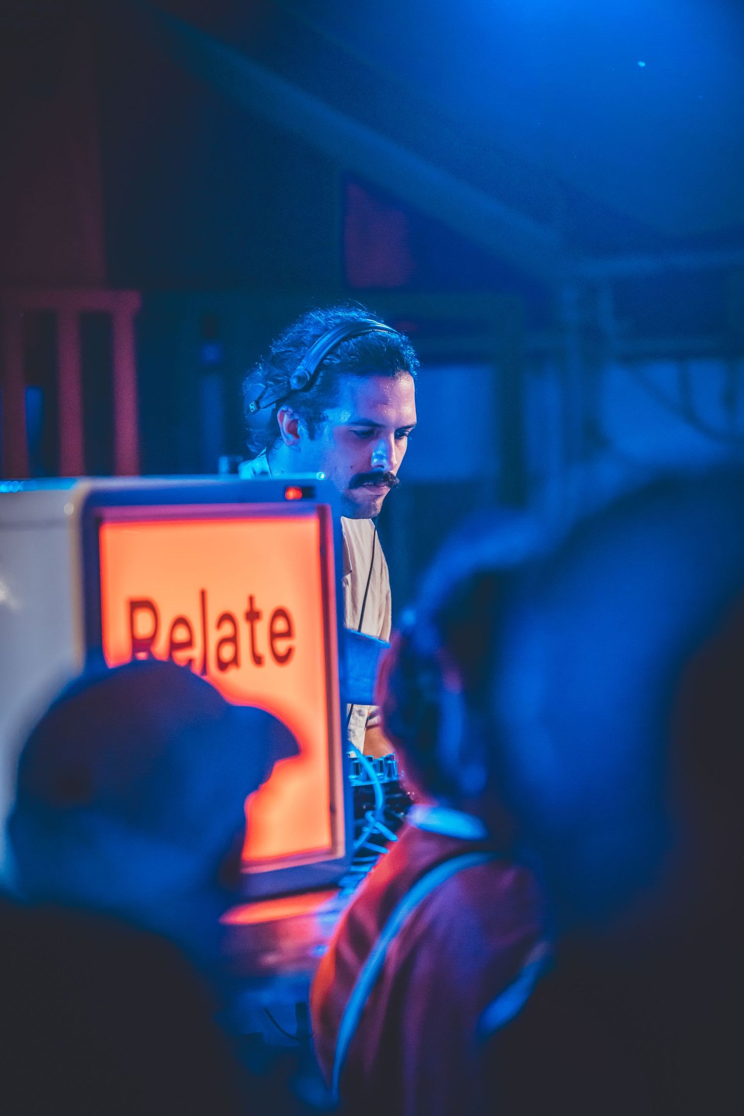 An artist performs at night under moody blue lighting with a 'Relate' sign visible in the foreground.