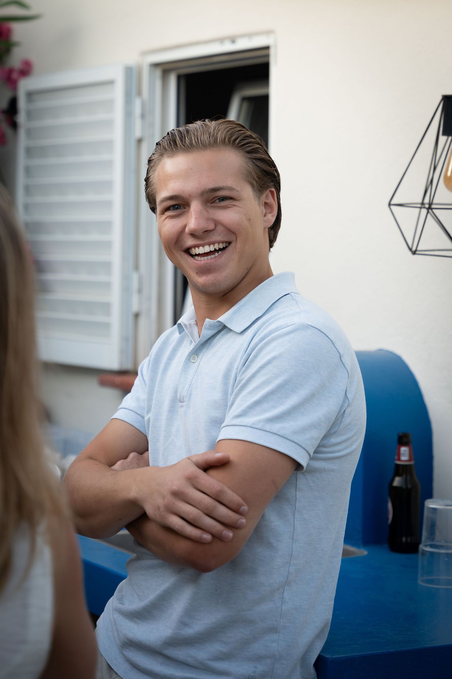 A collage sequence showing someone in a white polo shirt sitting against a blue wall while smiling and crossing arms.