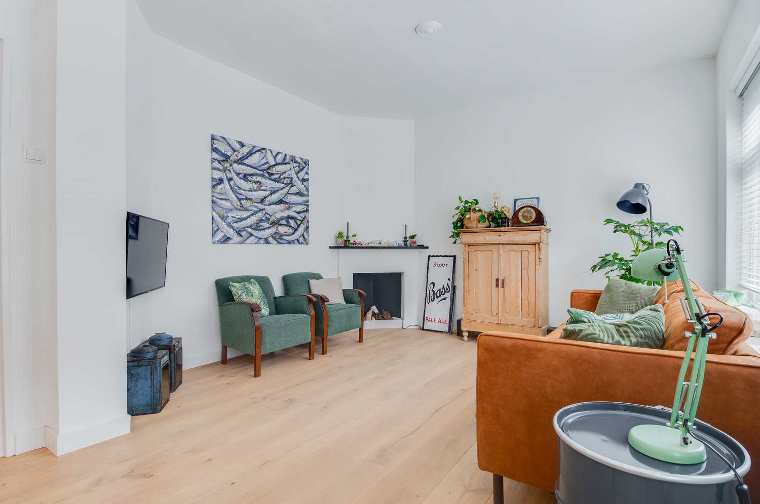 Modern living room with hardwood floors, teal accent chairs, tan leather sofa, and wall-mounted TV in white space.