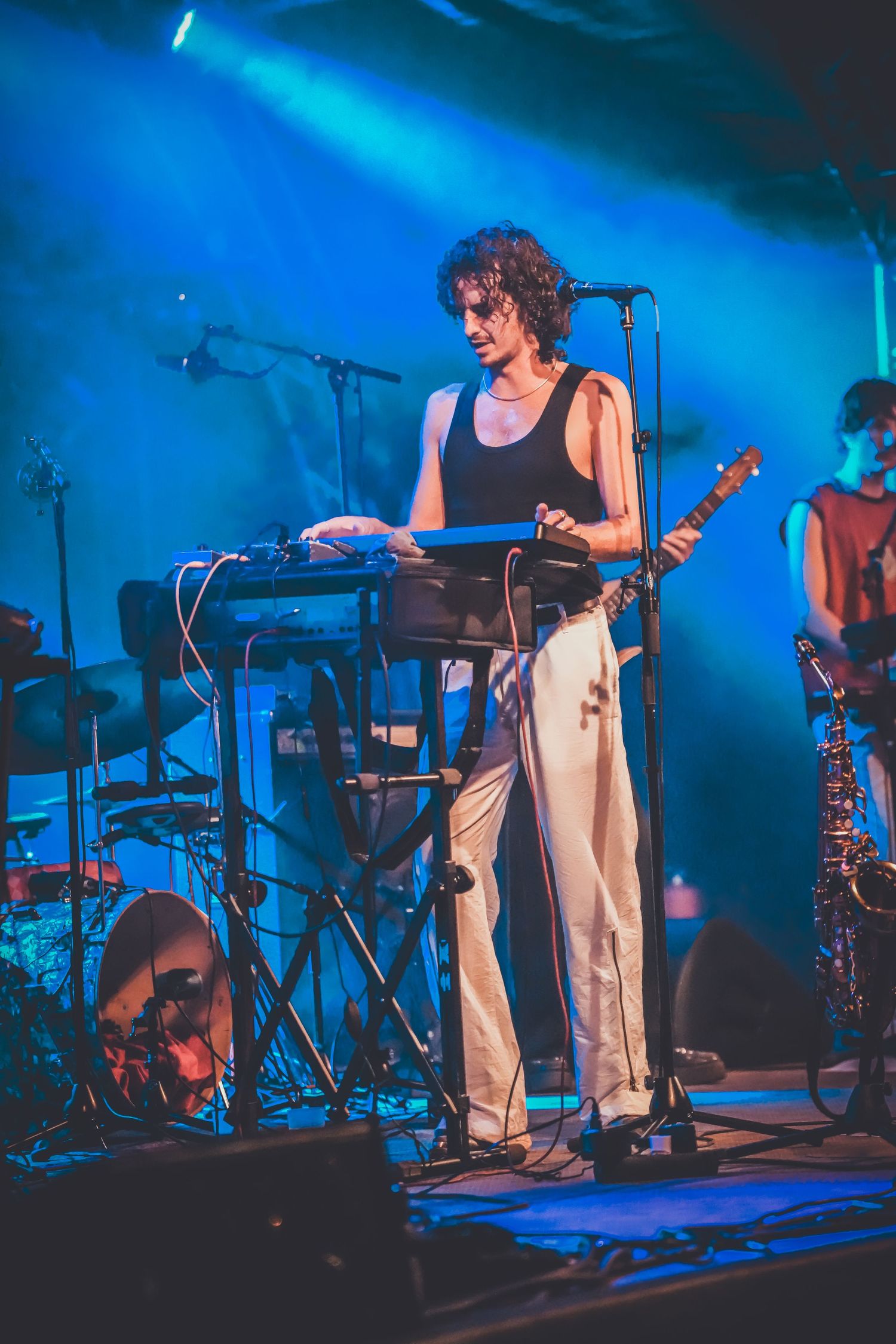 Musicians perform on stage with blue lighting and electronic instruments during a live concert.