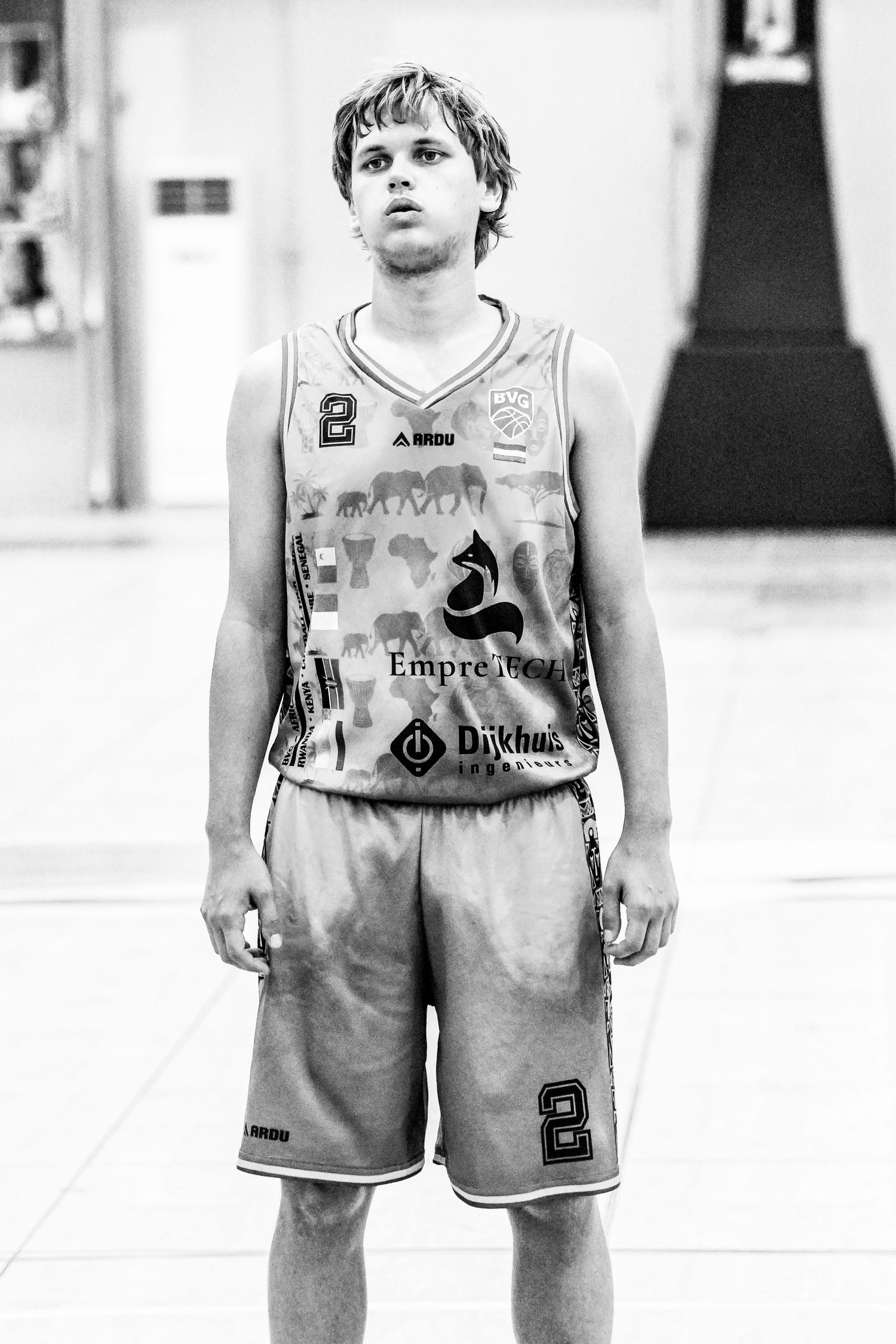 Young male basketball player in number 8 jersey standing on indoor court in black and white photo.