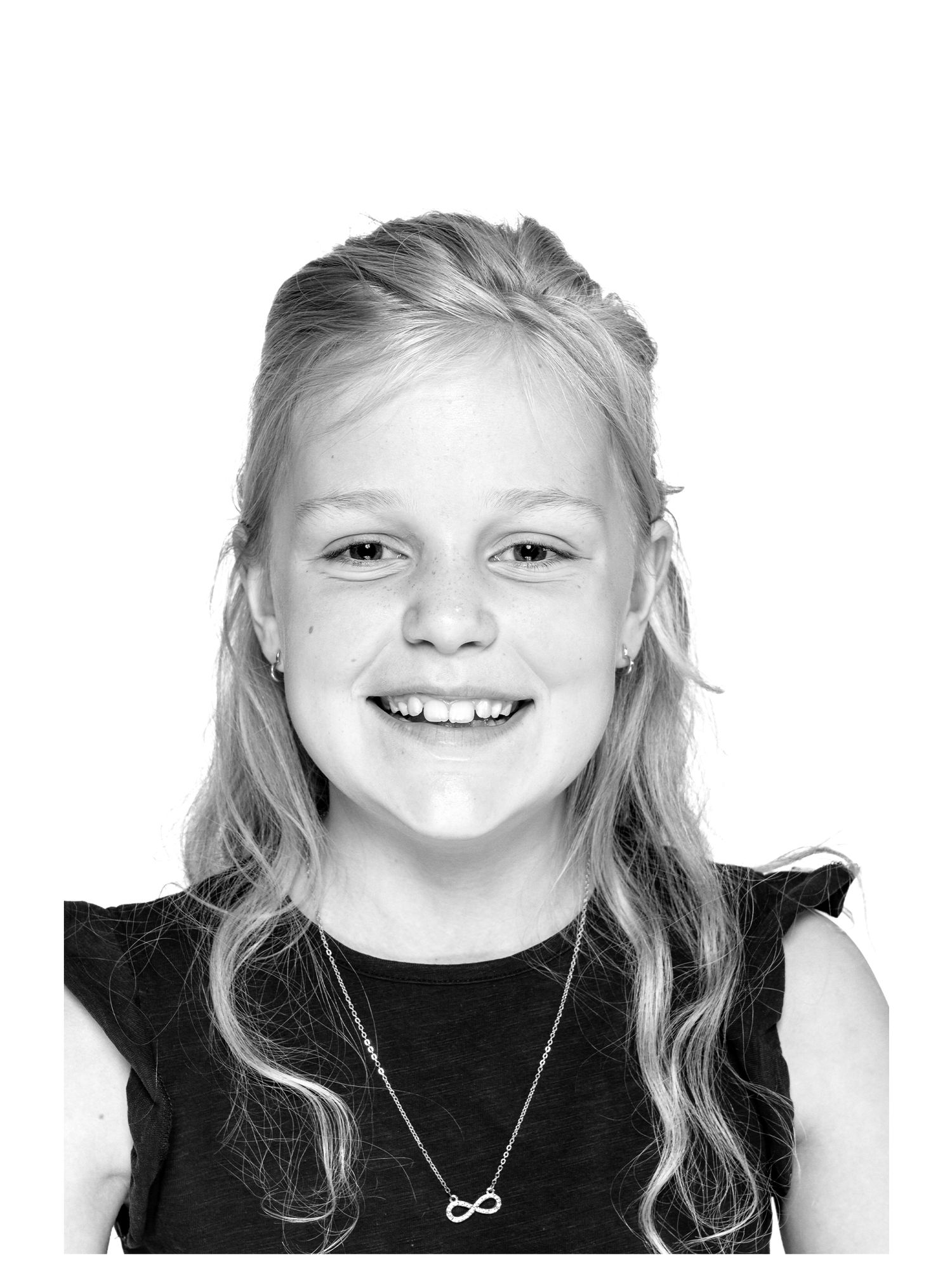 Black and white studio portrait of a joyful young person with long blonde hair and an infinity necklace against white background.