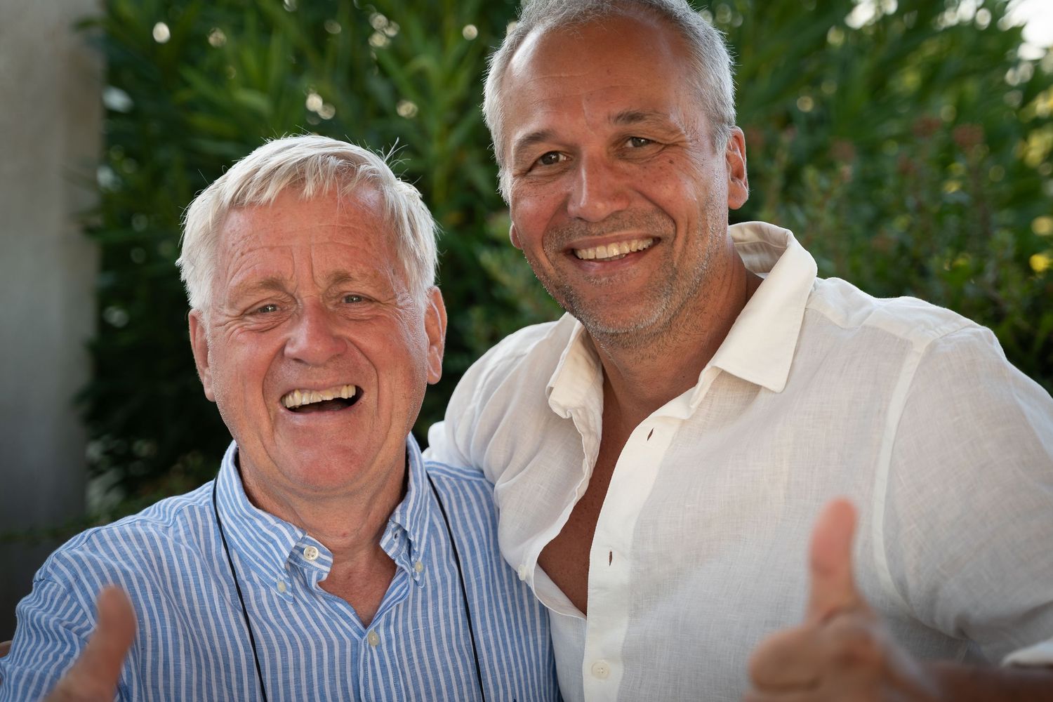 Two people in casual attire share a candid moment of laughter outdoors against a green background.
