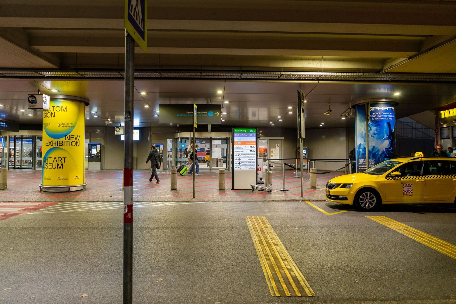 Yellow taxi waits at night in an underground parking garage with illuminated signage and yellow floor markings.
