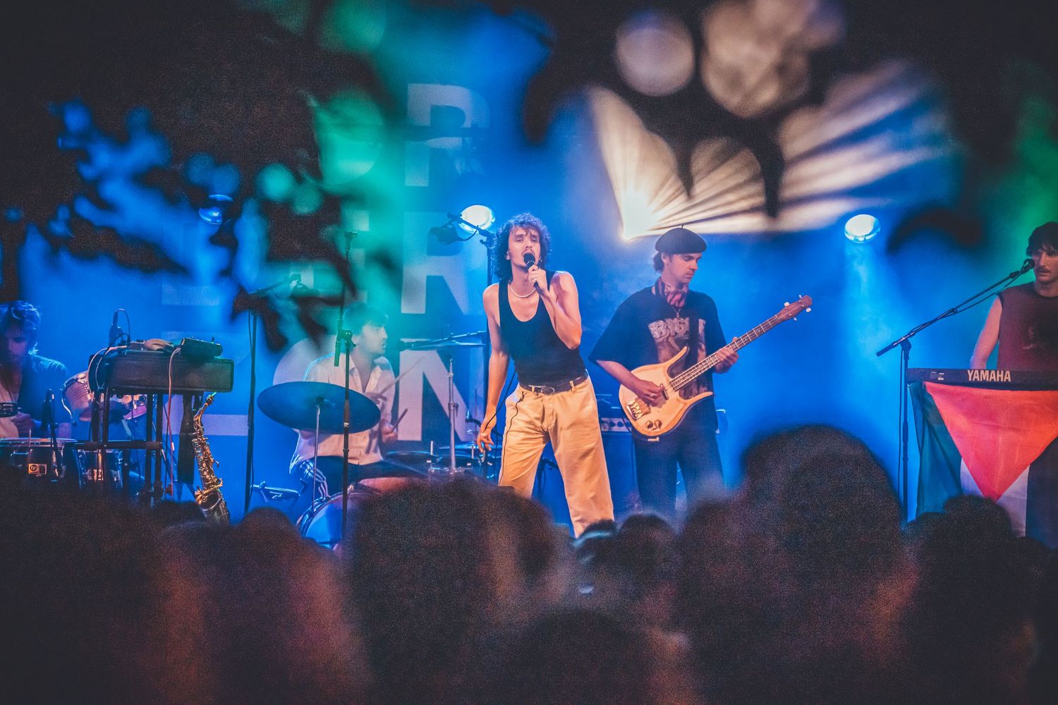 A concert performance on stage with dramatic blue and green lighting illuminating musicians performing live music.