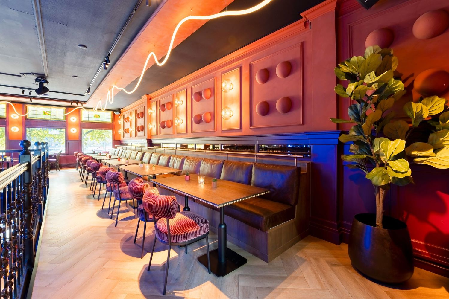 Vibrant restaurant interior with red booths, wooden tables, colorful chairs, neon lighting, and tropical plant decor.