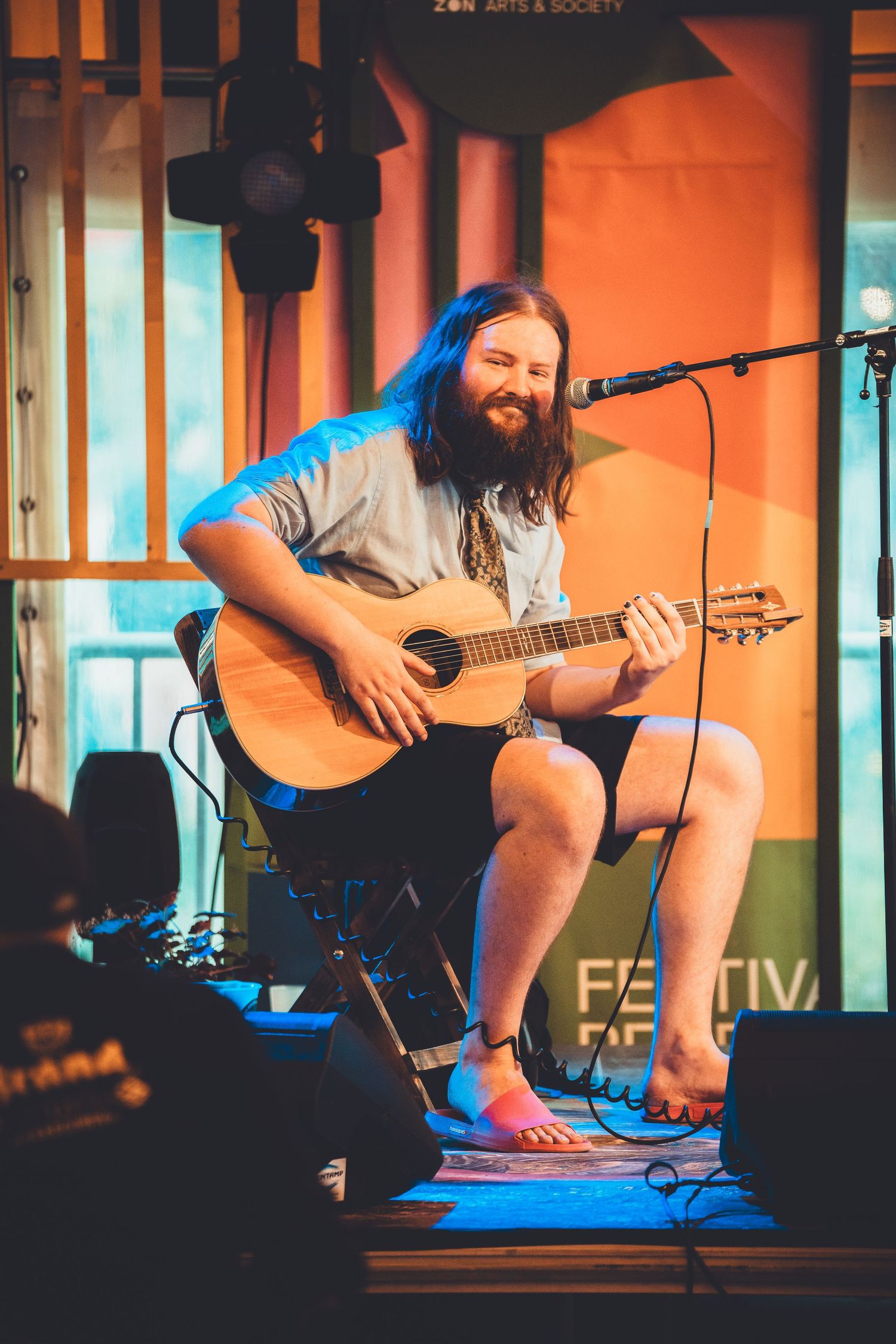 Musician performs on acoustic guitar on stage with warm lighting and microphone setup for live performance.