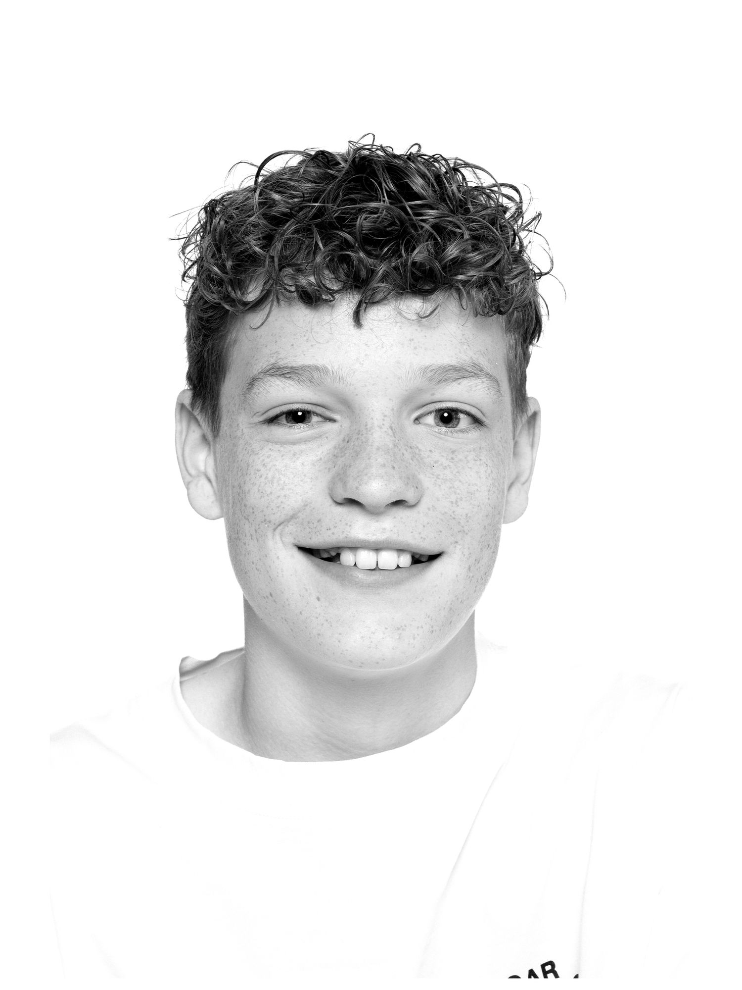 Black and white portrait photograph showing a young person with curly dark hair and a friendly smile against a light background.