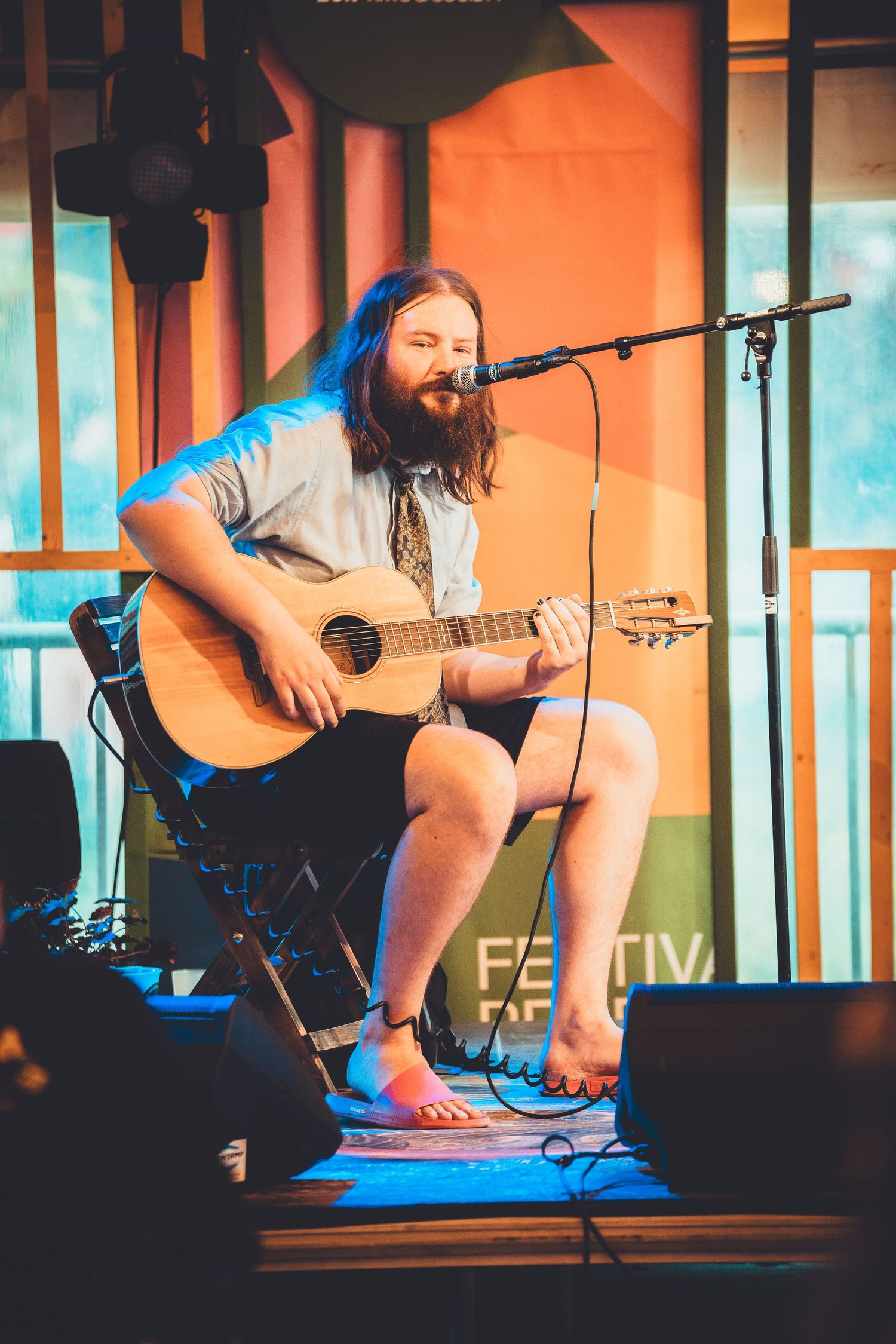 An acoustic guitar performance on stage with warm orange lighting and blue accents during a live music show.