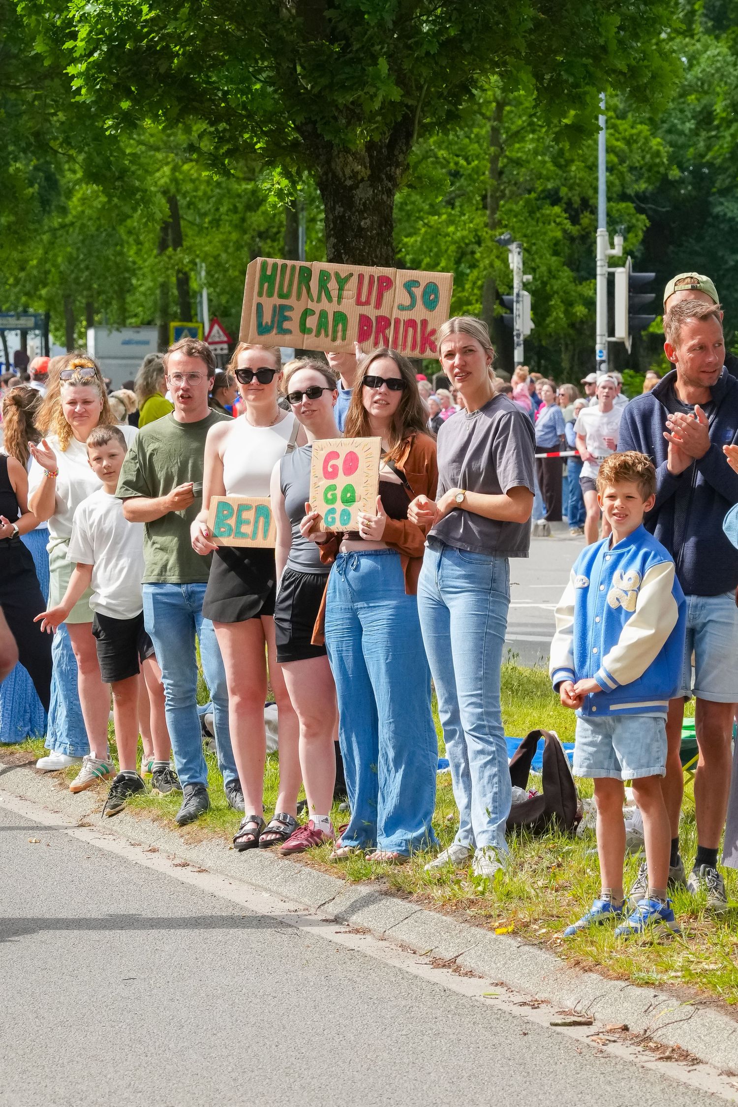 Crowd of spectators lining a road holding signs including 