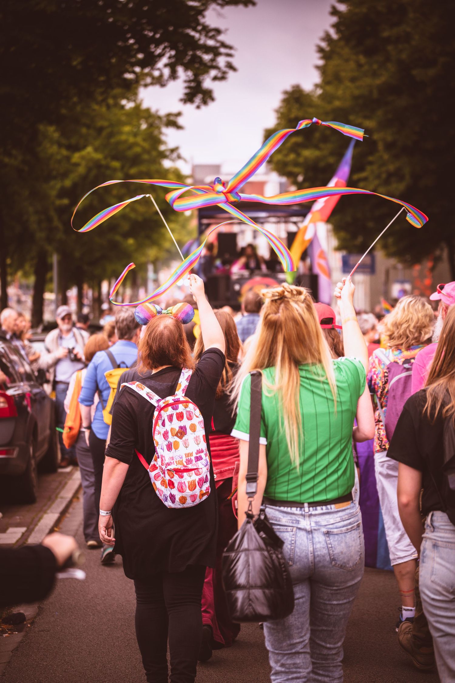 Crowd of people walking down a street waving flags and ribbons during a pride celebration event.
