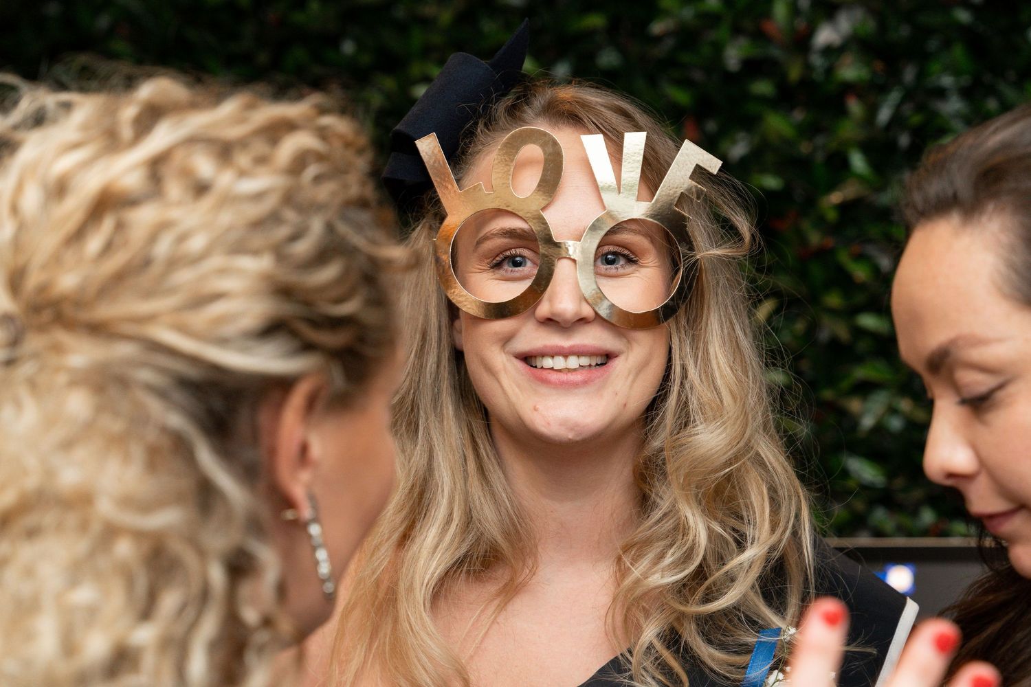 A group of wedding guests laugh and smile together while wearing sunglasses outdoors.