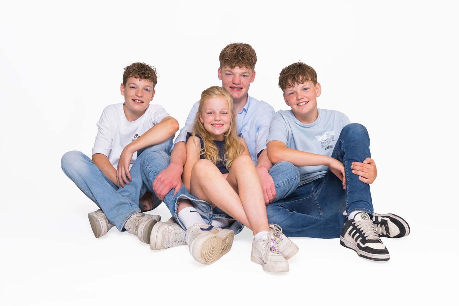 Five youth sit together in casual outfits and white socks while laughing and socializing.