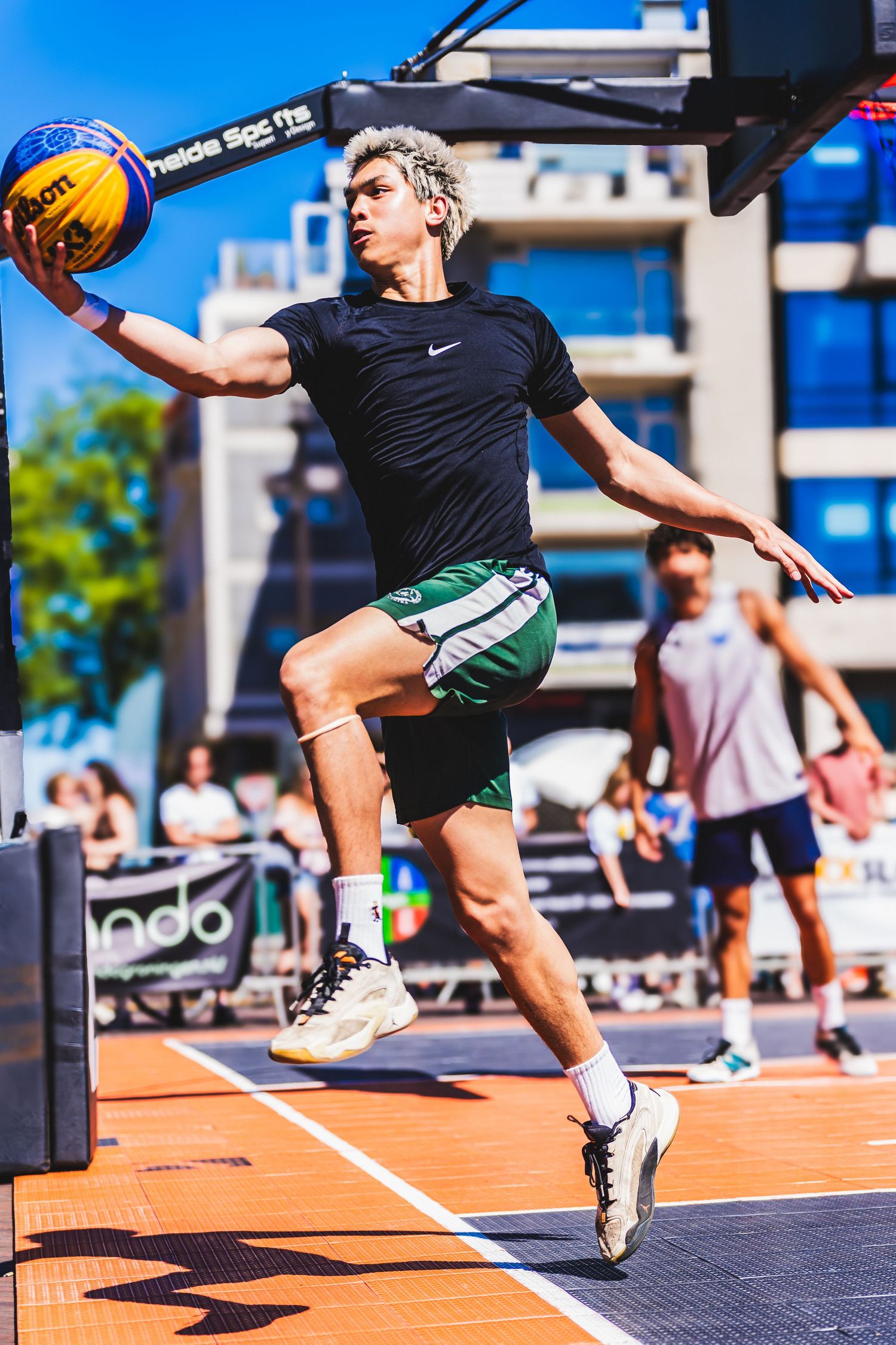 Young athlete in Nike gear dunks basketball on outdoor court during a sunny 3x3 street basketball tournament.
