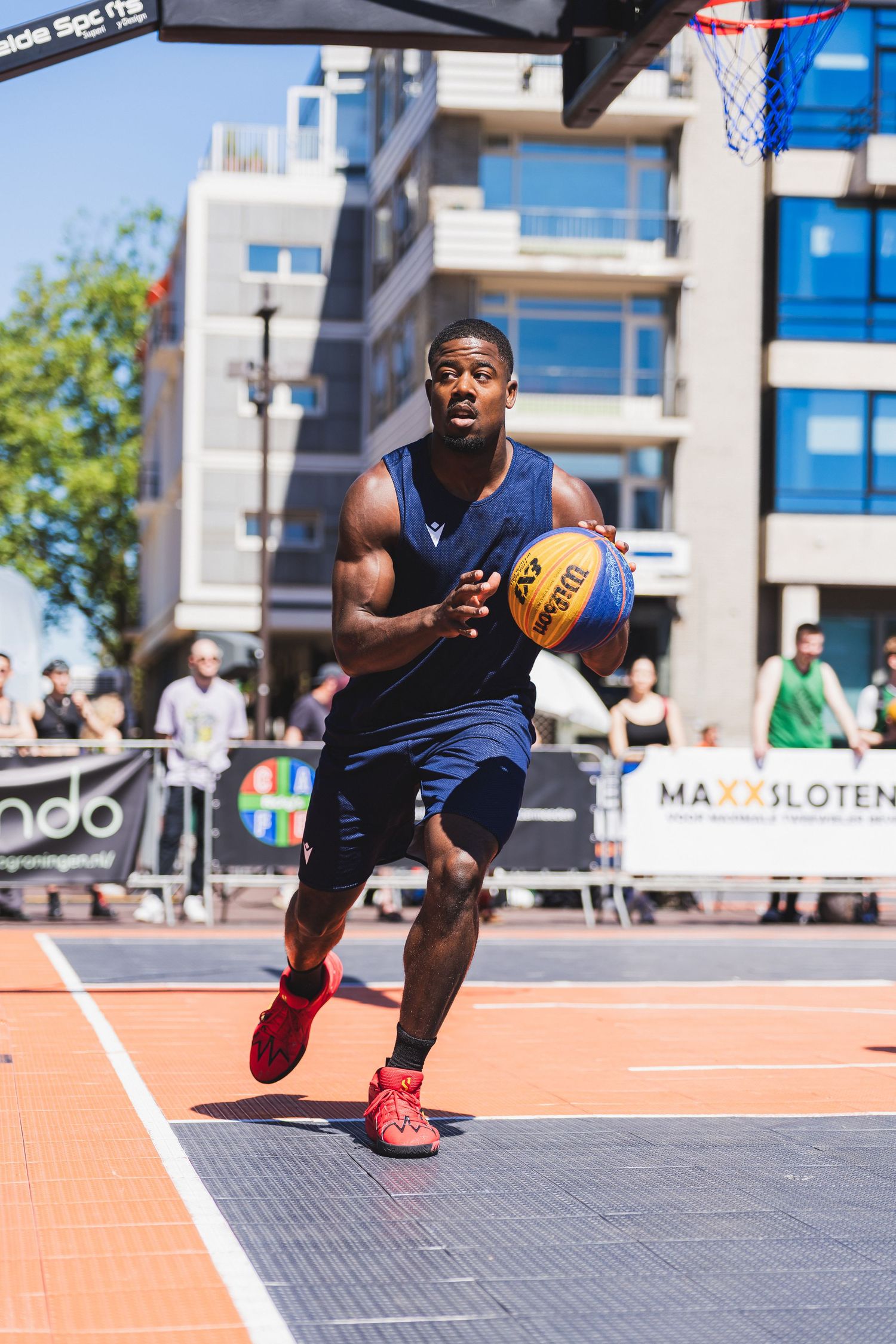 A young male basketball player dribbles on an outdoor 3x3 court during a sunny urban tournament.