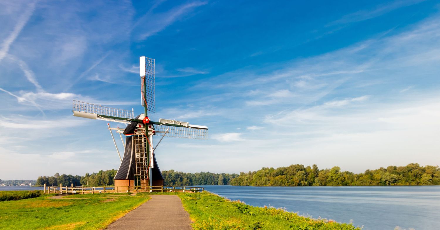 Traditional Dutch windmill along a canal with green grass and vibrant blue sky in Netherlands.