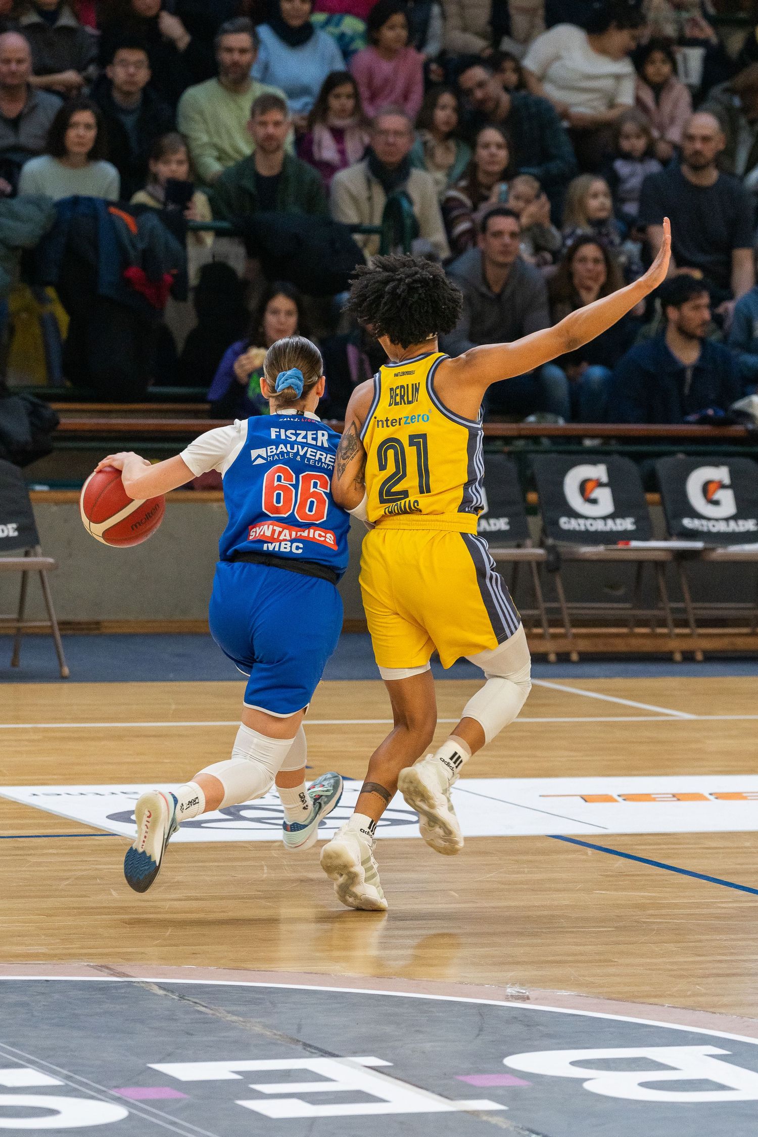 Two basketball players compete for the ball during an intense game, one in blue jersey 86 and another in yellow 21.