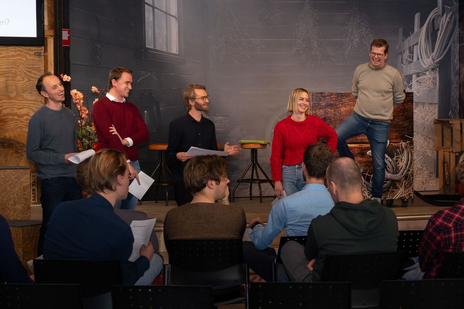 A group of people sitting and standing in a casual indoor setting during what appears to be a workshop or meeting.