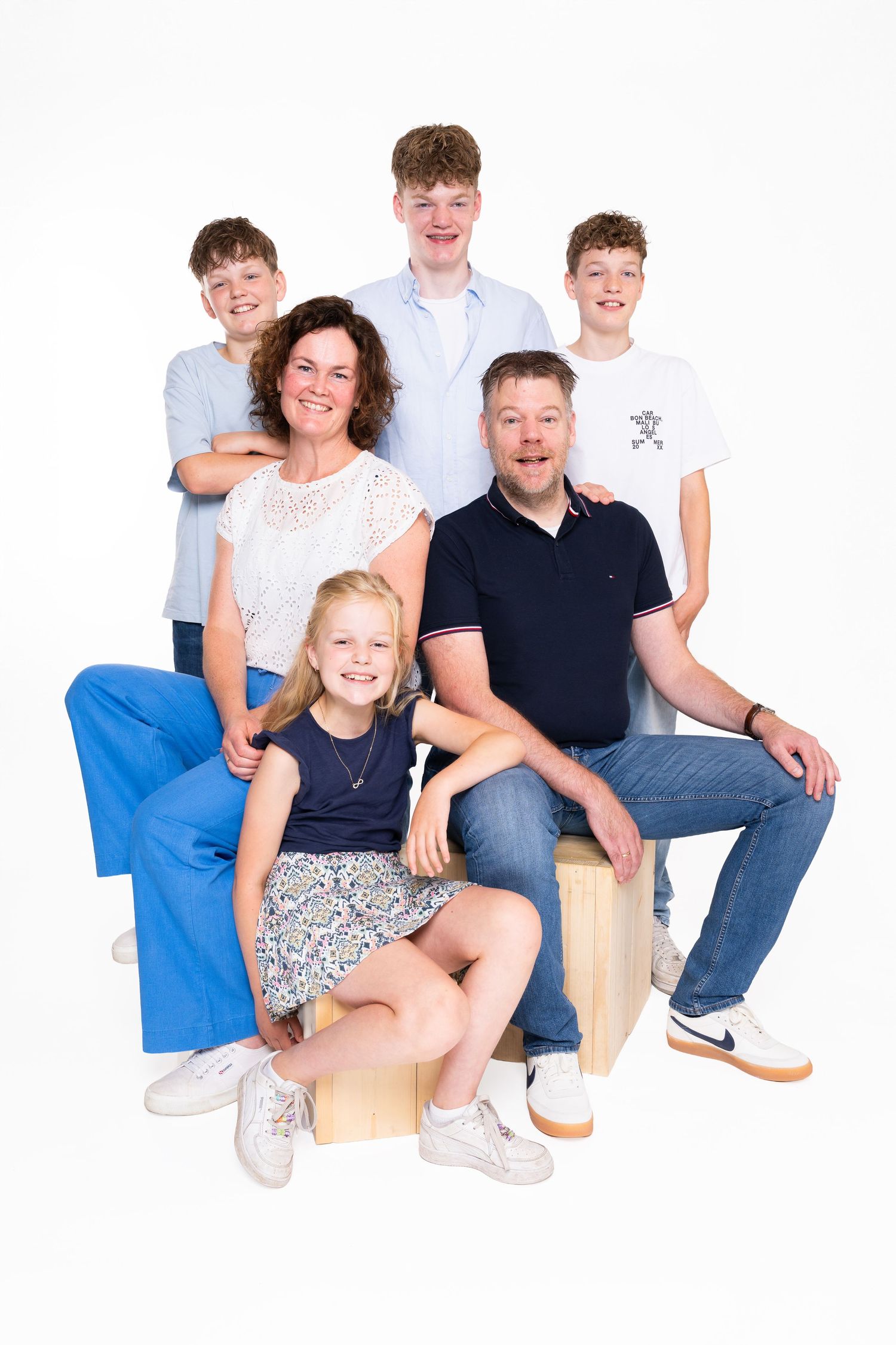 A group sits together on wooden blocks wearing casual attire in a bright studio setting for a family portrait.