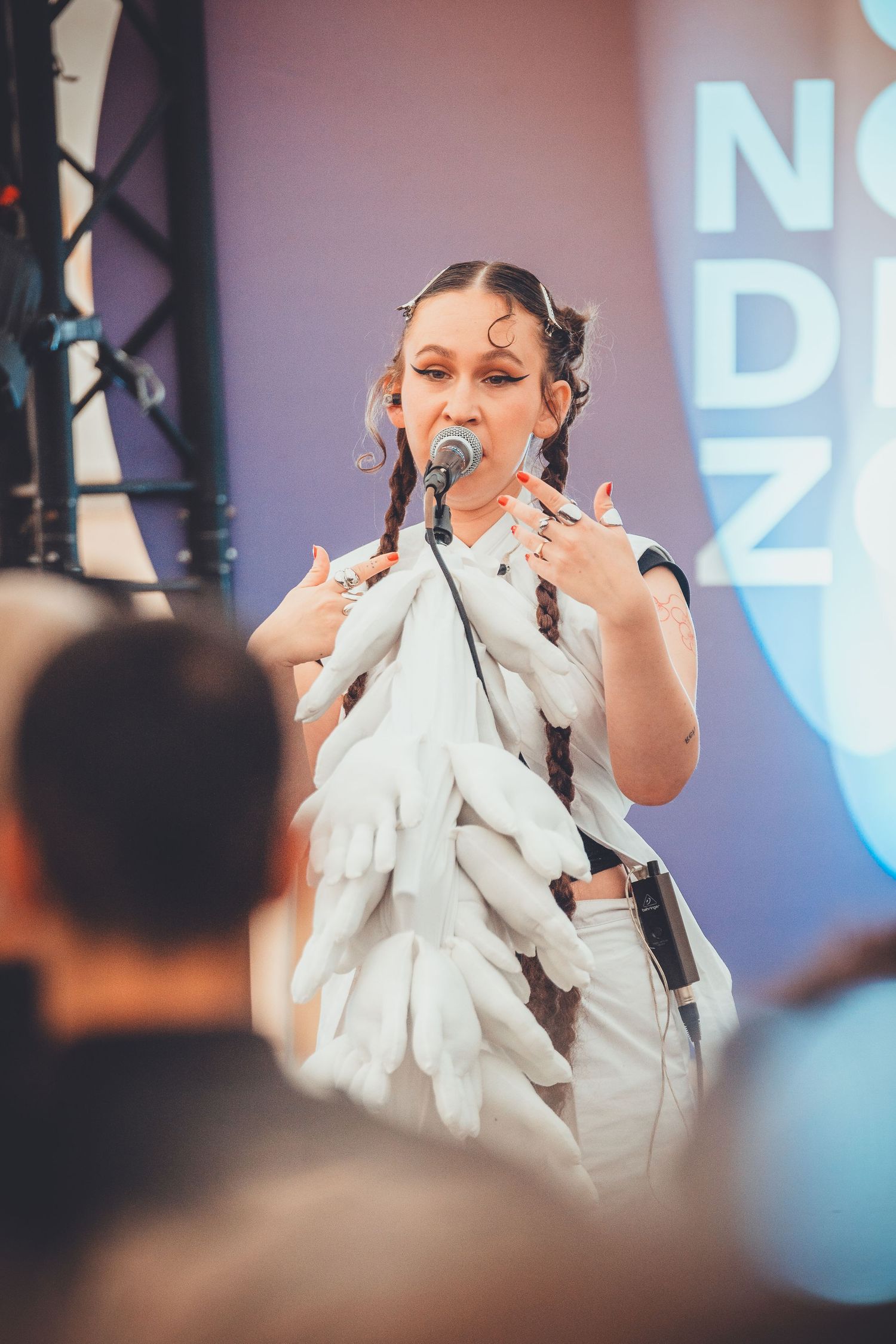 A performer in a white feathered outfit sings emotively on stage during a live concert performance.