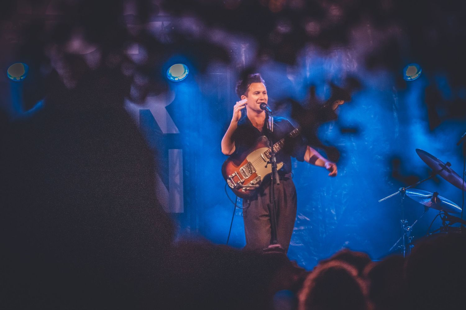 A musician performs on stage with a guitar amid dramatic blue lighting and smoke effects during a concert performance.