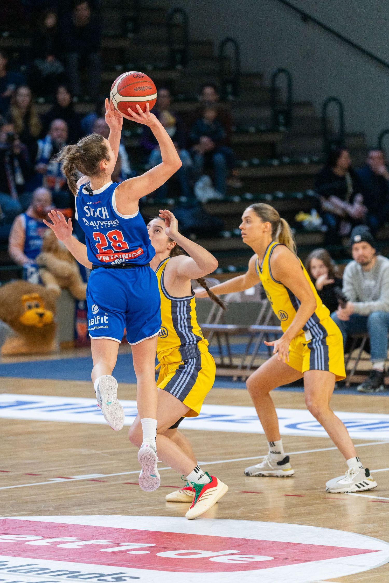 Basketball player in blue jersey falls while defending against opponent in yellow uniform during indoor game.