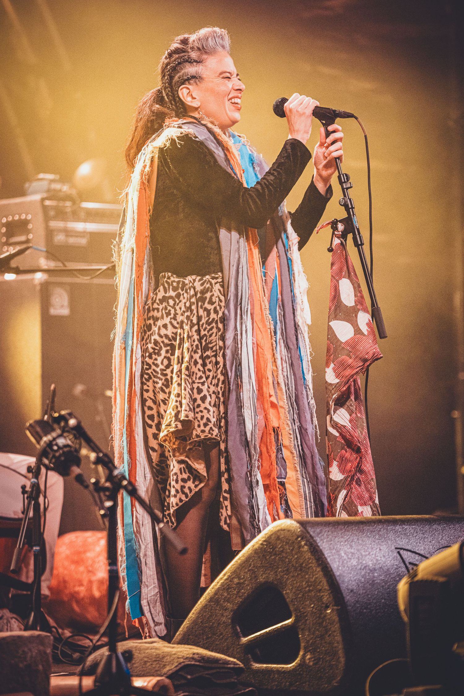Performer in leopard print dress and colorful scarf sings on stage with dramatic lighting.