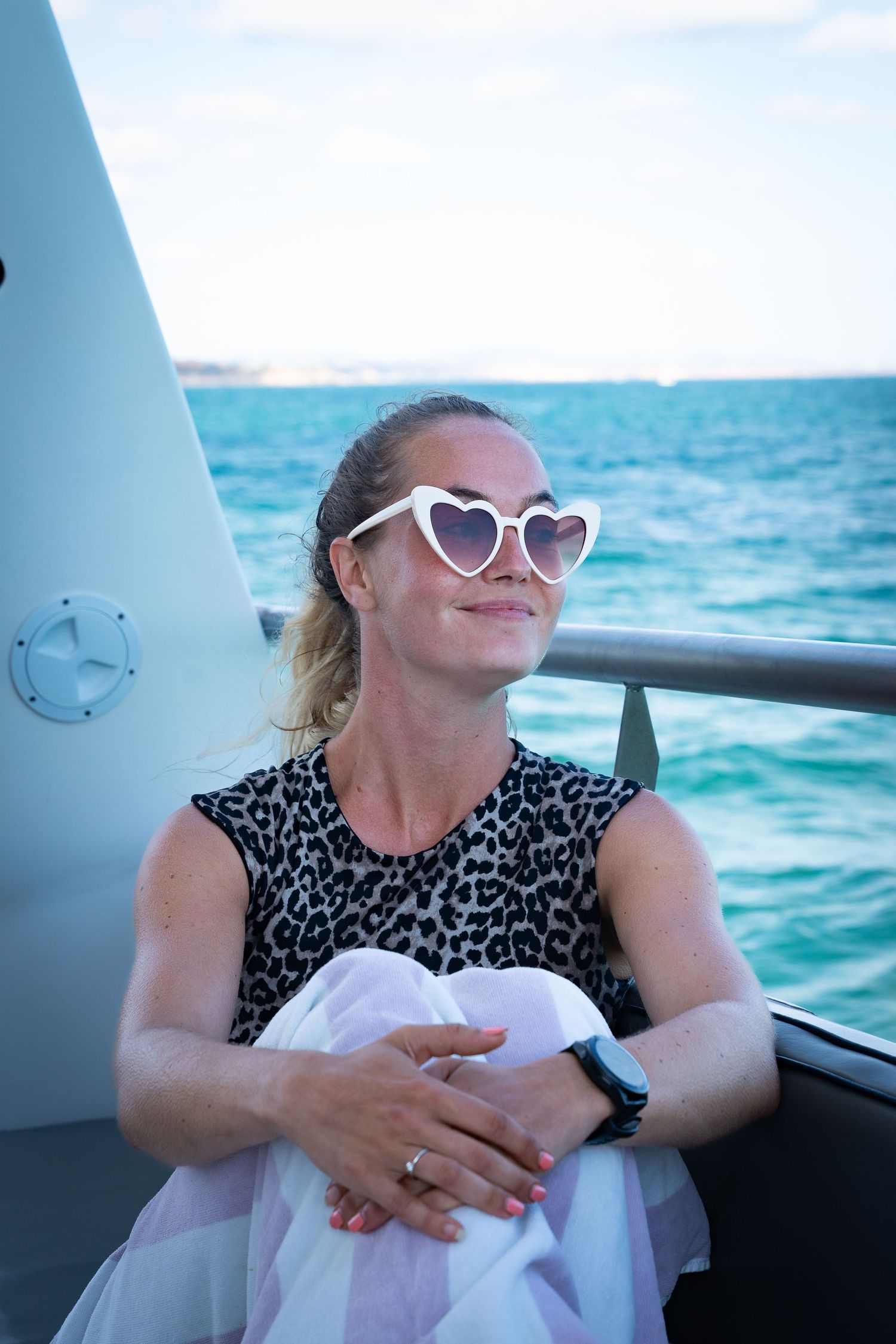 Someone wearing heart-shaped sunglasses and a leopard print top relaxes on a boat with turquoise ocean waters in the background.