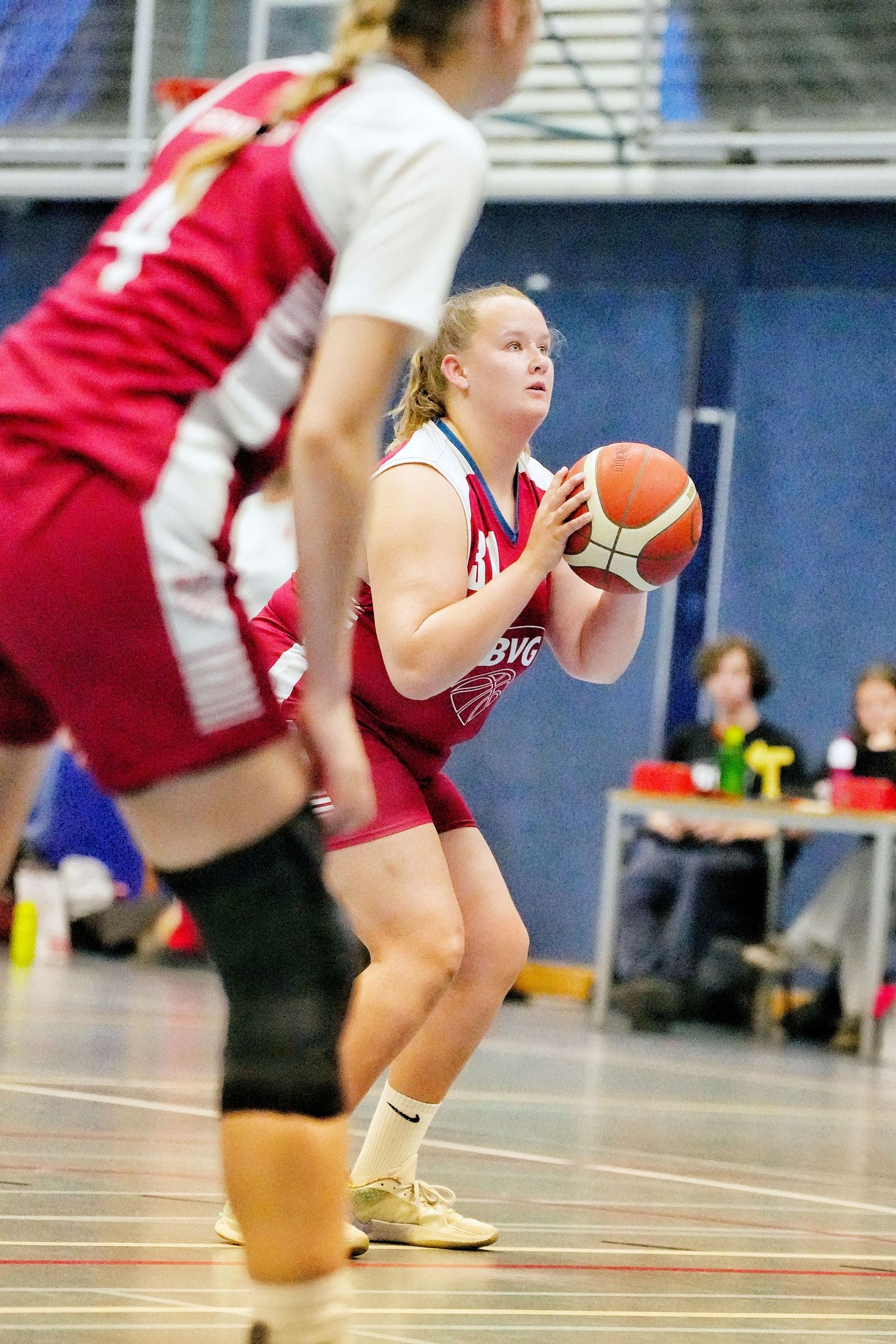 Female basketball player in red uniform prepares to shoot during an indoor game.
