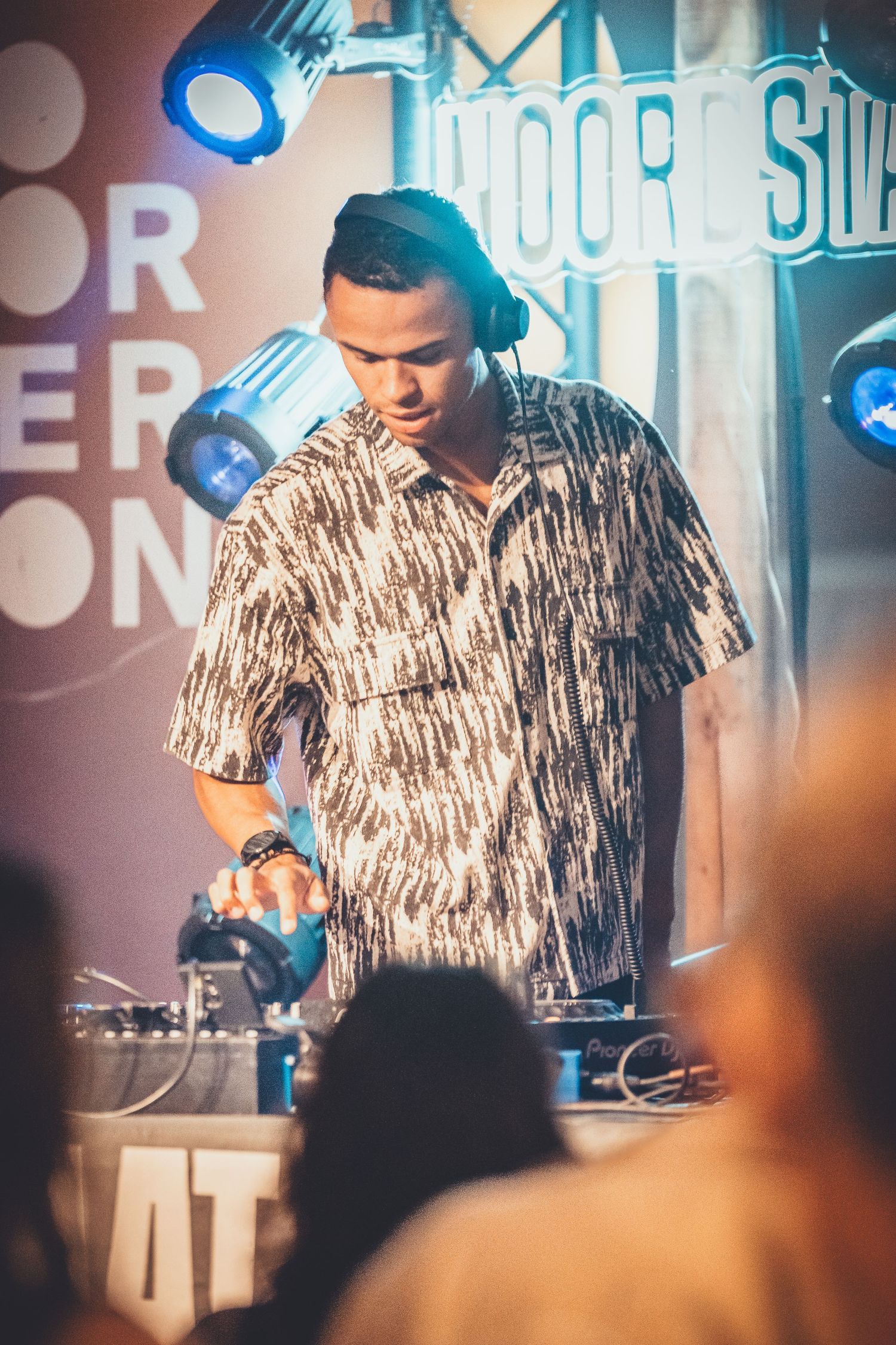 DJ performs on stage with turntables under blue lighting at a nightclub event.
