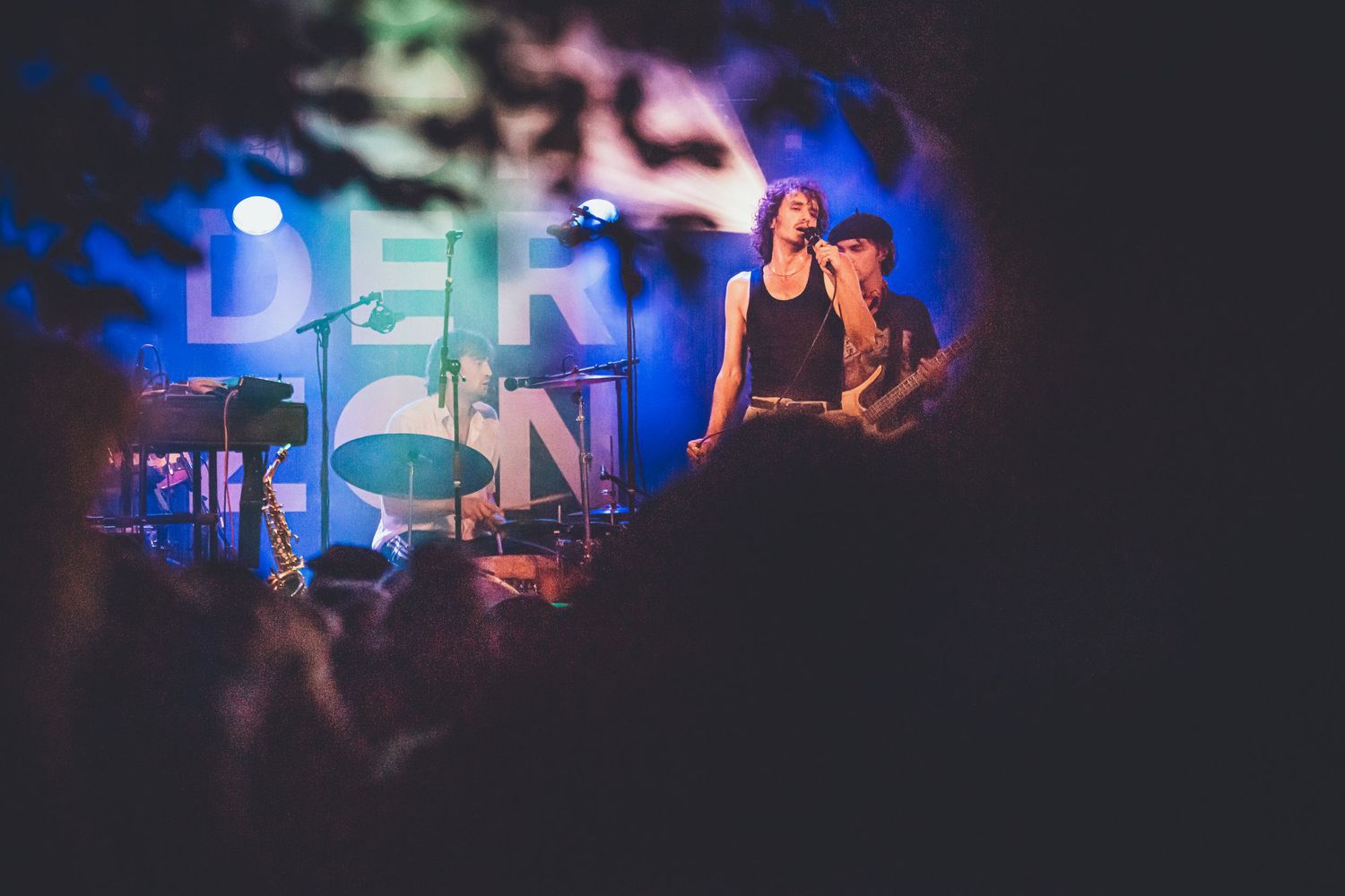 A performer on stage at a concert with moody blue lighting and 'BERLIN' text visible in the background.