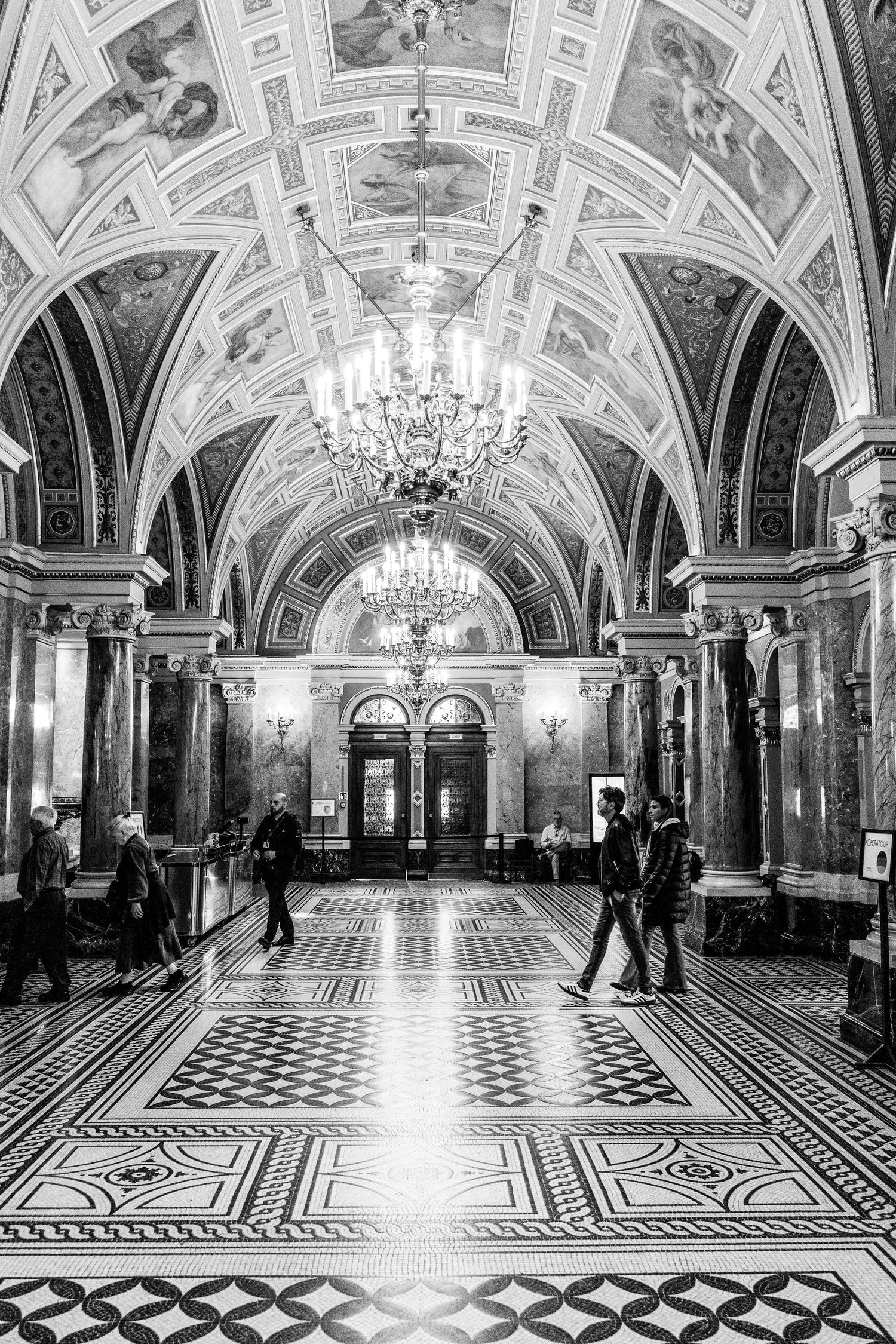 Ornate grand hall with vaulted ceilings, crystal chandeliers, and geometric marble floor patterns in a historic palace.