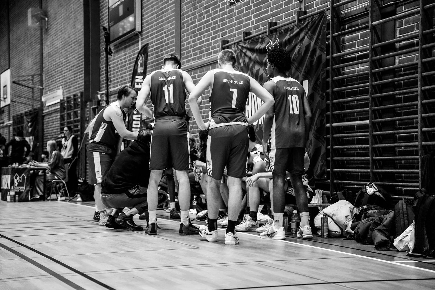 Black and white photo of basketball players wearing jerseys numbered 11, 7, and 10 huddling on a court.