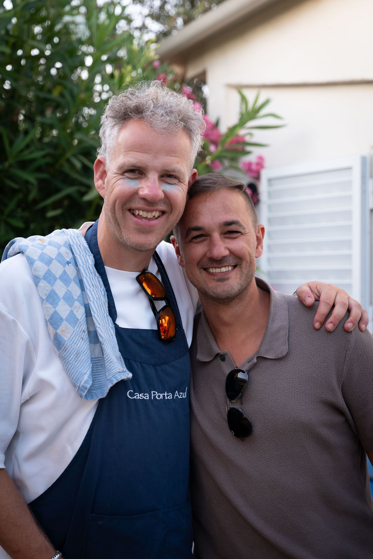 Two smiling people in casual attire posing together outdoors with greenery in the background.