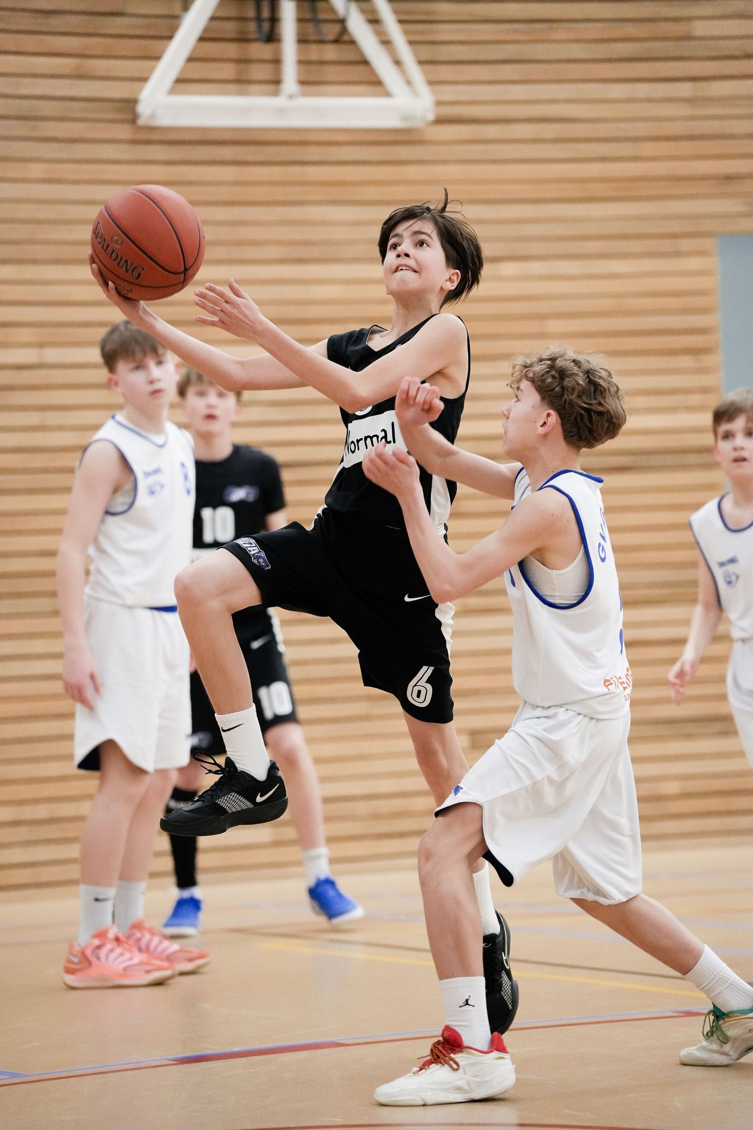 Young basketball player in black jersey drives to the basket during a youth league game in an indoor court.