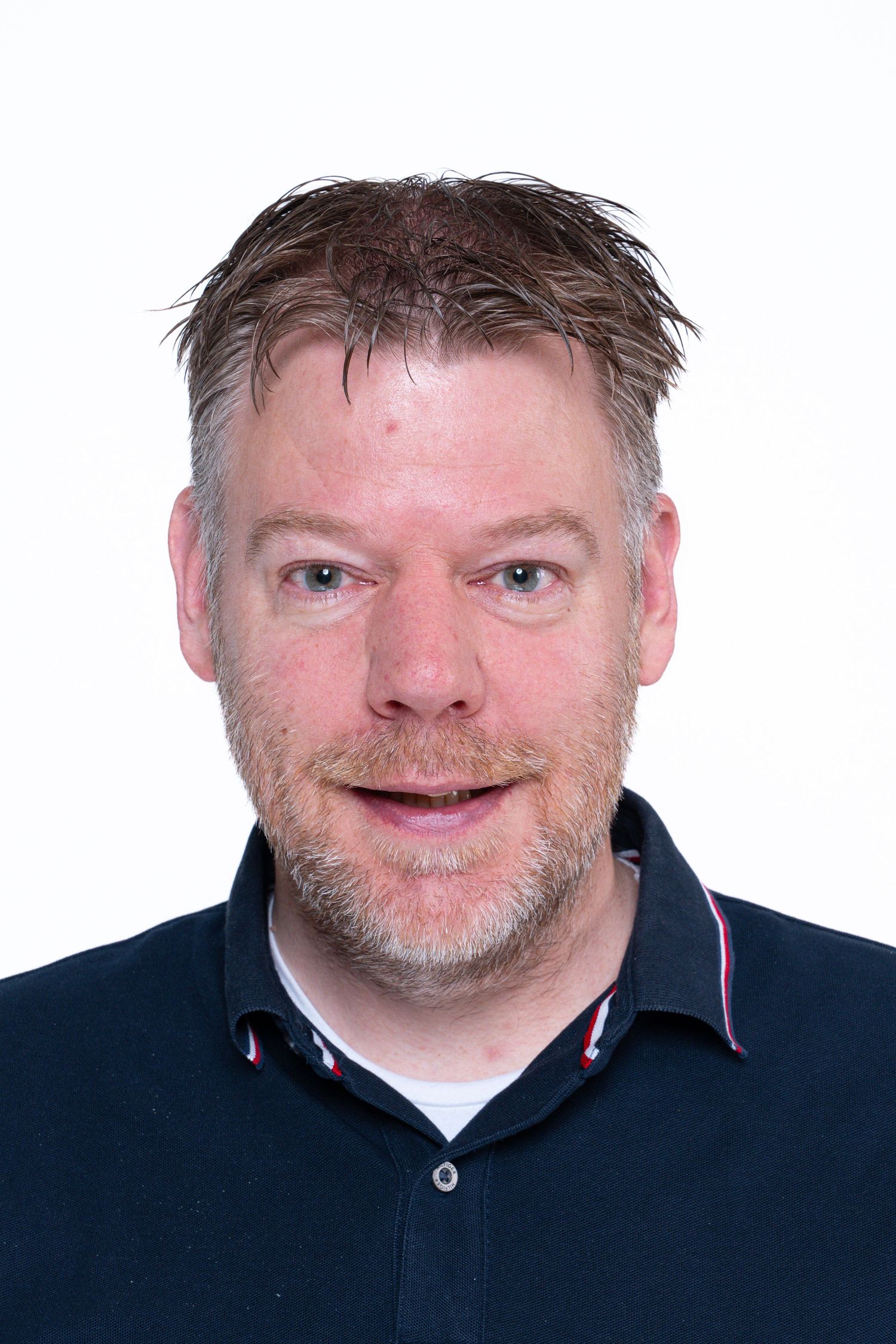 Head and shoulders portrait of a person with strawberry blonde hair wearing a navy polo shirt against white background.