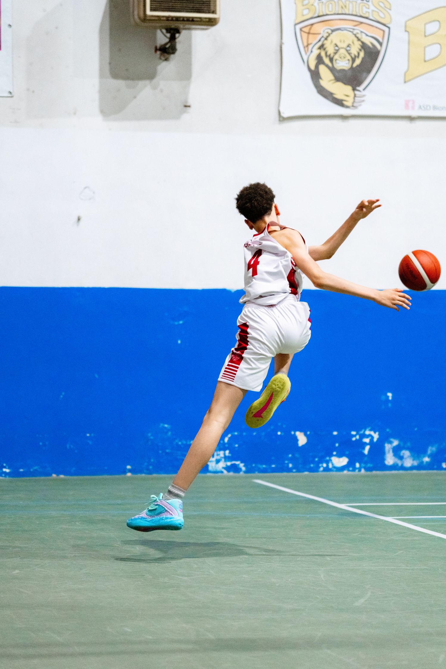 Young basketball player in white uniform leaping to catch an orange ball on an indoor court.