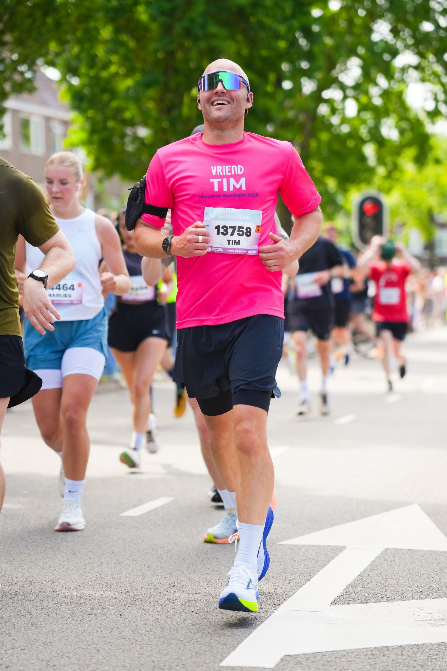 Man named Tim wearing pink shirt and bib number 13758 smiling while running in a road marathon race.