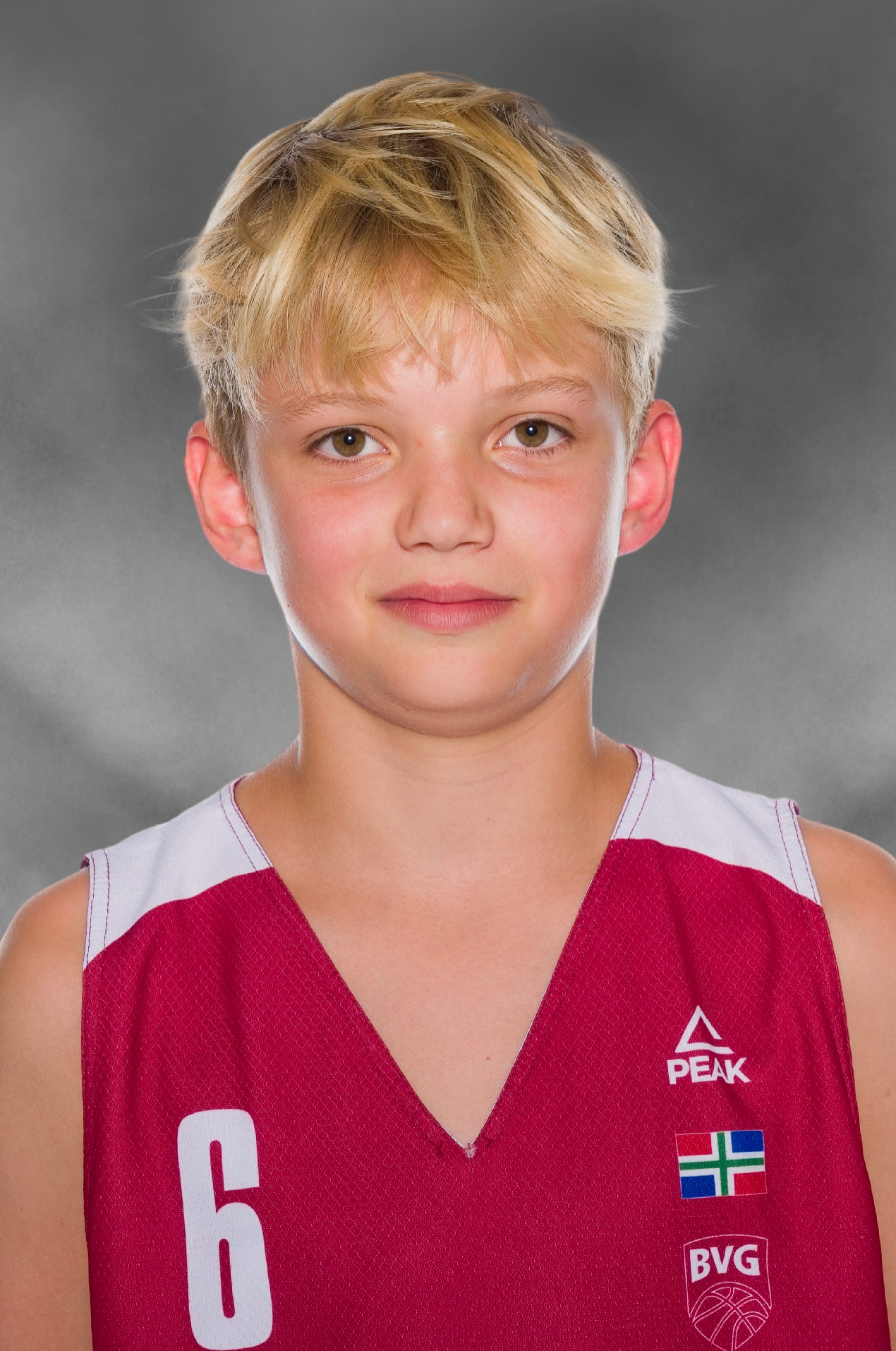 Young blond basketball player in a red number 6 Peak jersey with BVG logo posing for a team portrait against a gray background.