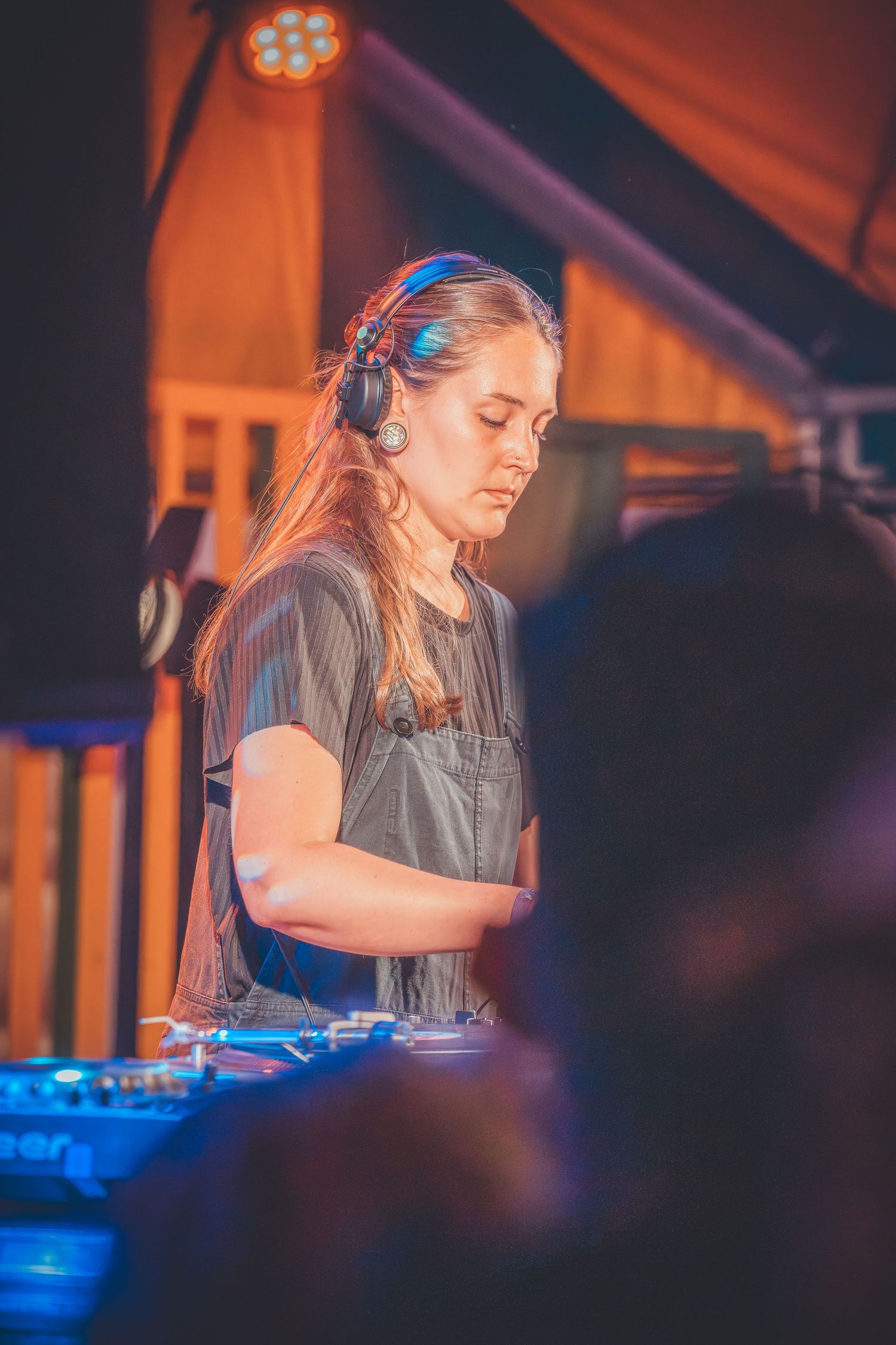 DJ performs at nightclub with mixing equipment under dramatic blue and orange lighting effects creating an atmospheric mood.