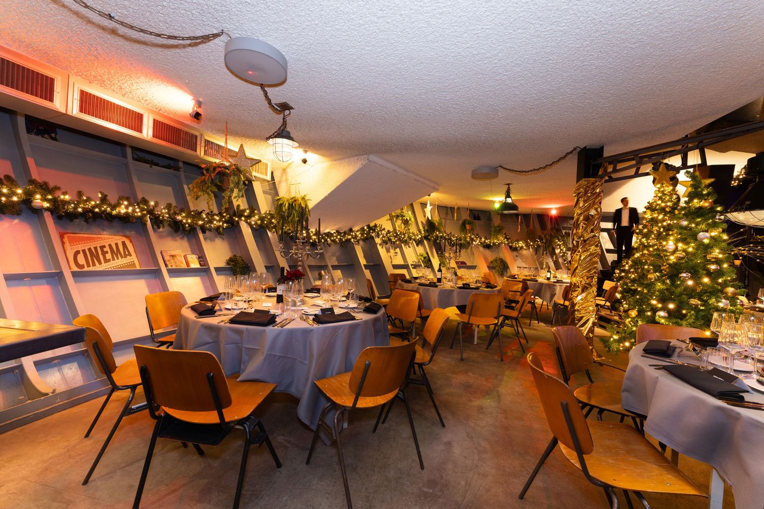 Elegant restaurant interior with decorated tables, chairs and Christmas trees creating a cozy holiday atmosphere.