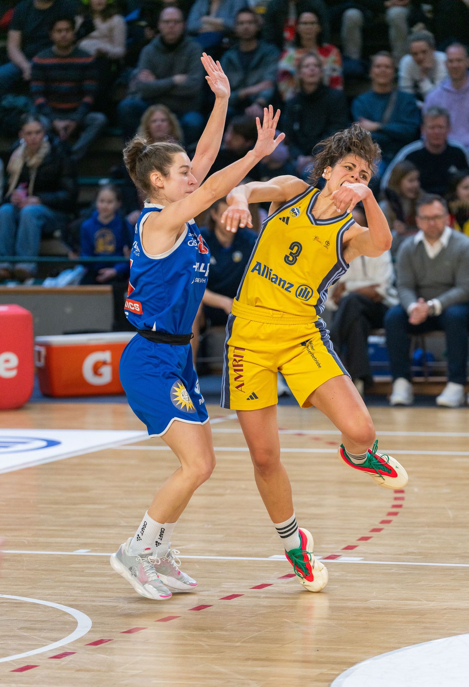 Two female basketball players compete intensely during a game, one in blue and one in yellow number 3 jersey.