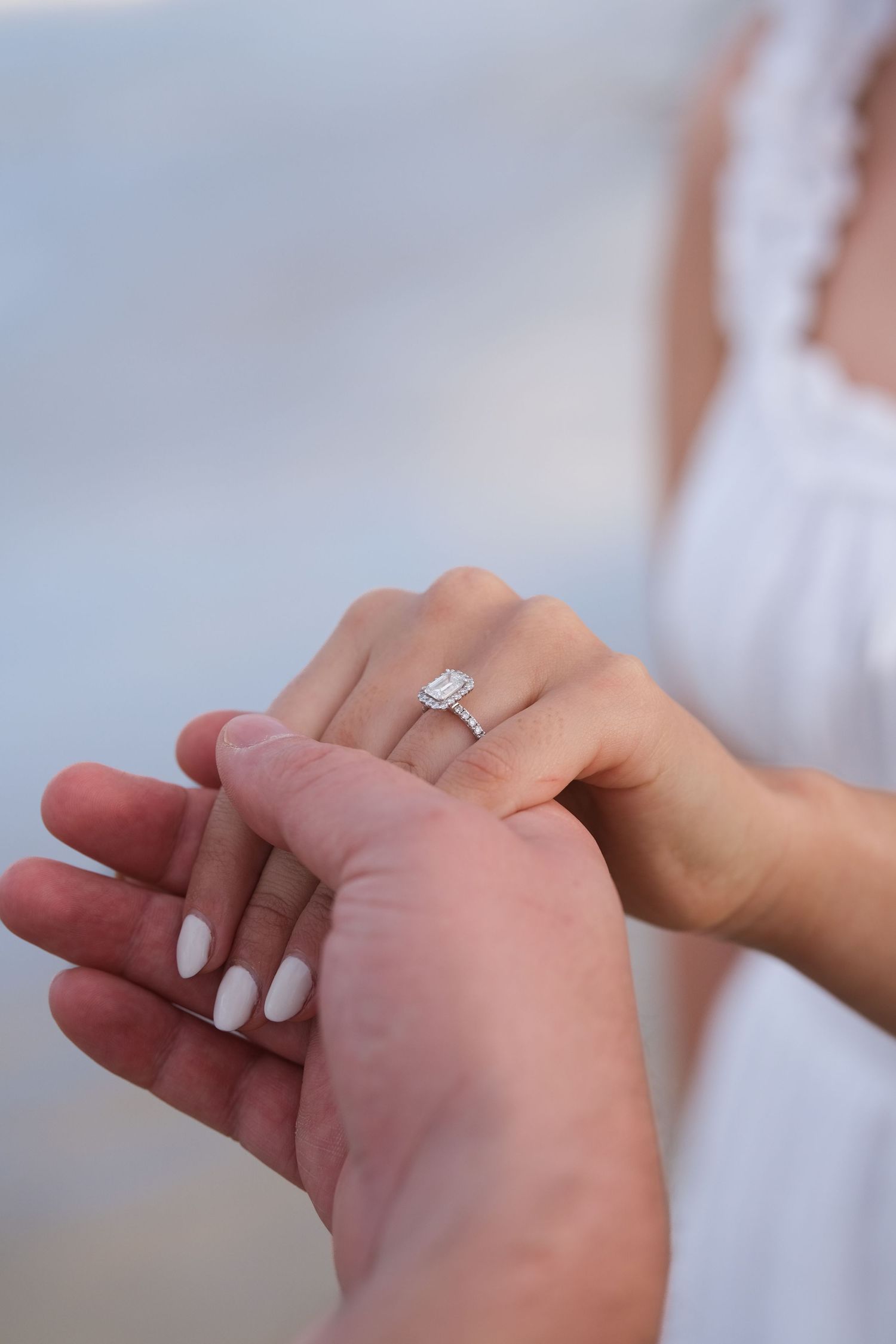Close-up of elegant emerald-cut diamond engagement ring on woman's hand held by her partner outdoors.